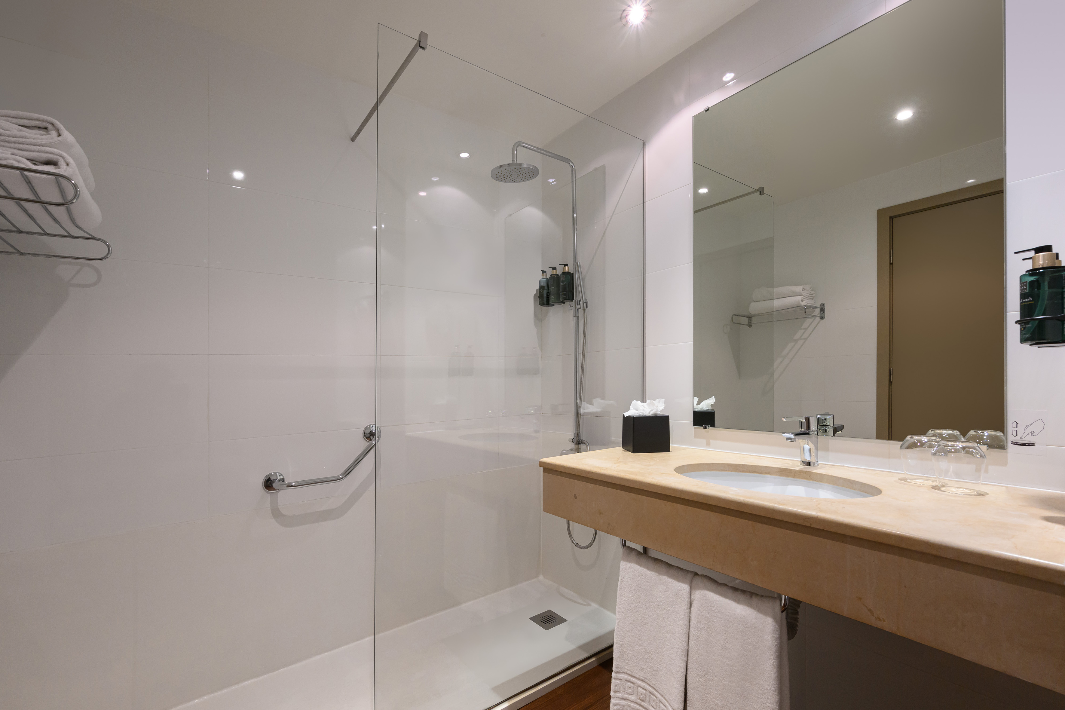 Modern hotel bathroom with walk-in shower, rain head, vanity, and mirror.