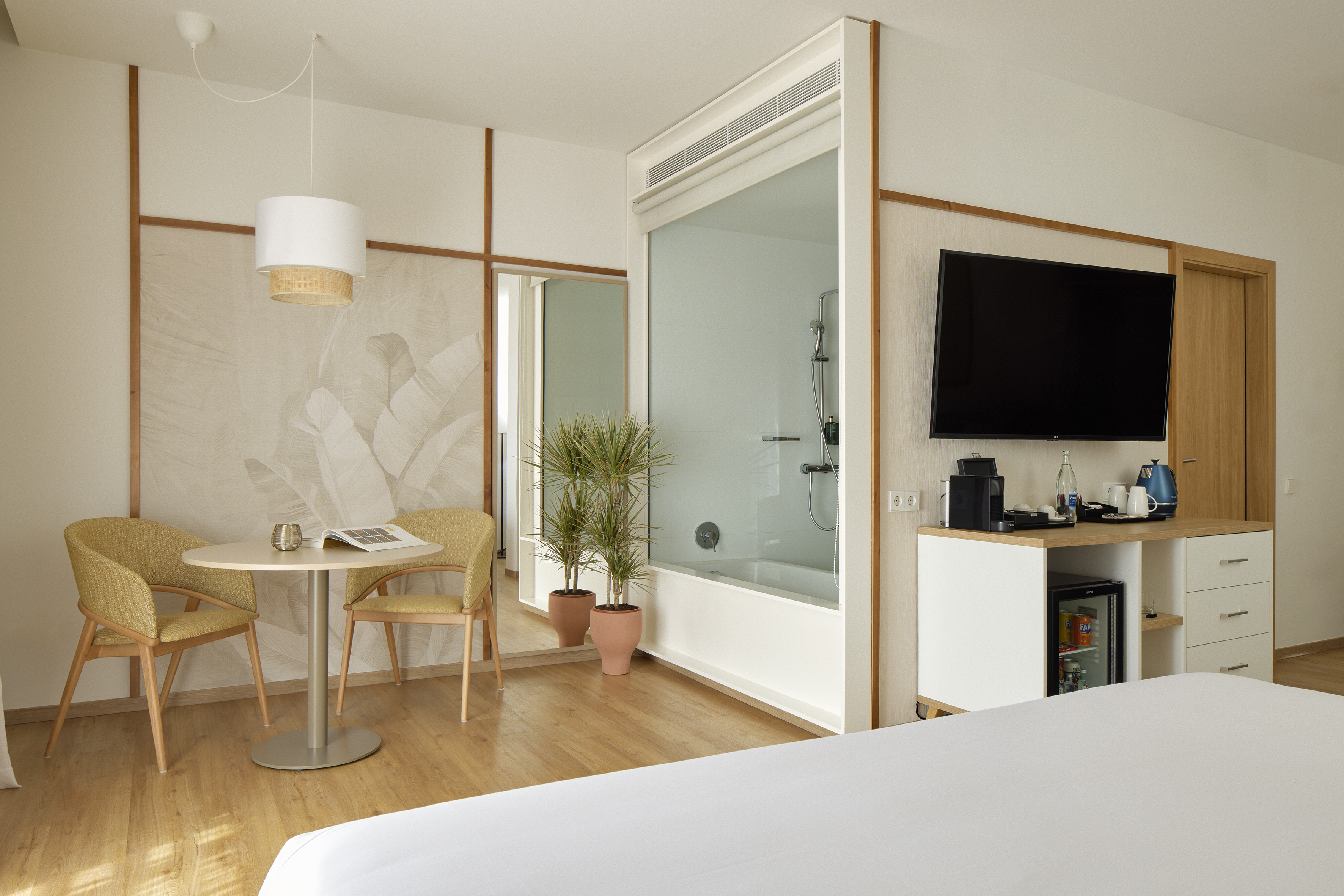 Contemporary hotel room with bed, seating, TV, and a glass-walled shower.