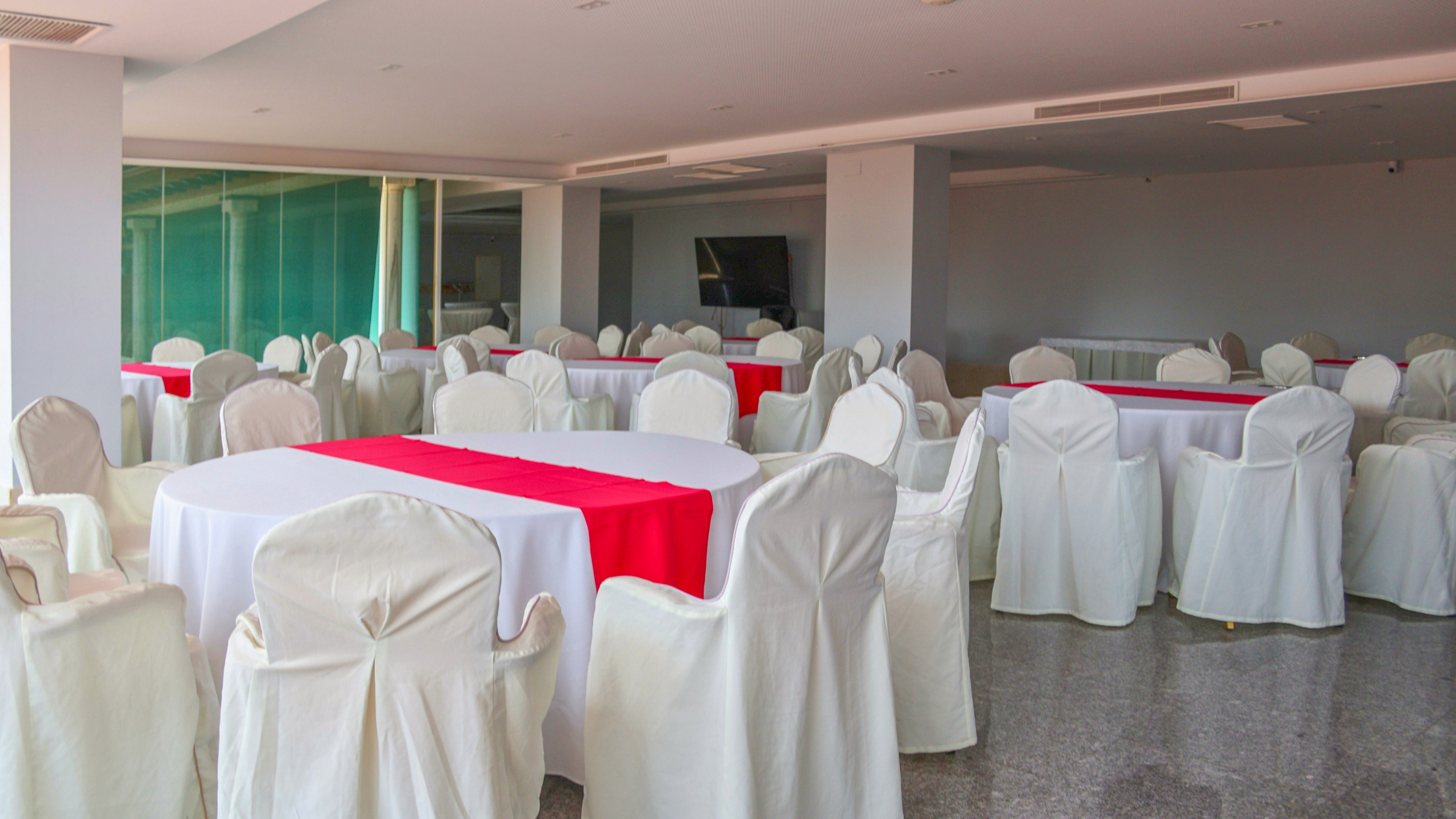 Empty conference room with round tables, white linens, red runners, and chair covers.