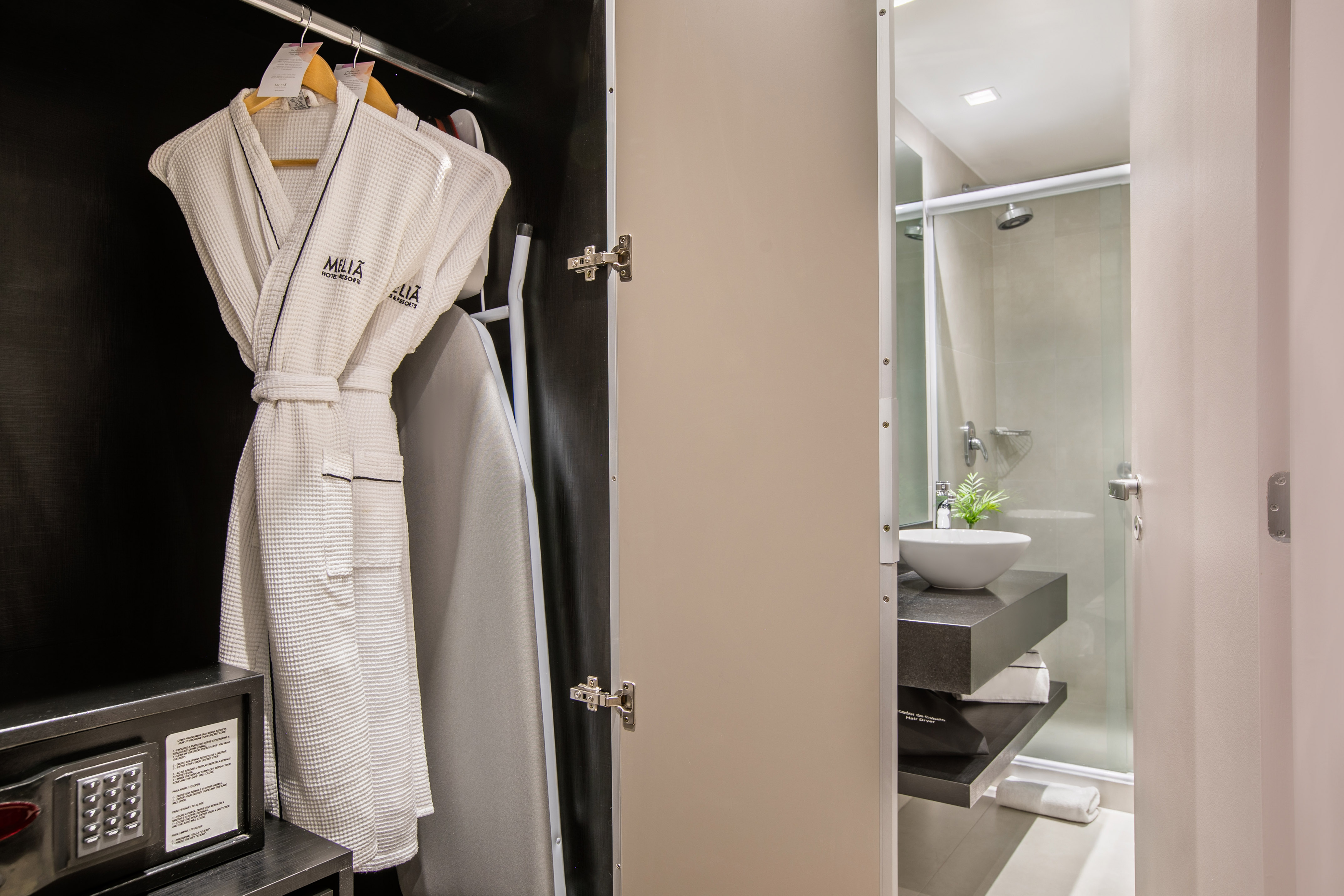 Meliá hotel closet with white bathrobes, safe, and modern adjacent bathroom.
