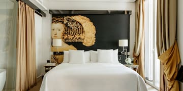 a bed with white sheets and pillows in a room with a large painting on the wall