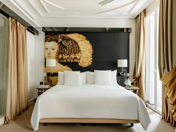 a bed with white sheets and pillows in a room with a large painting on the wall