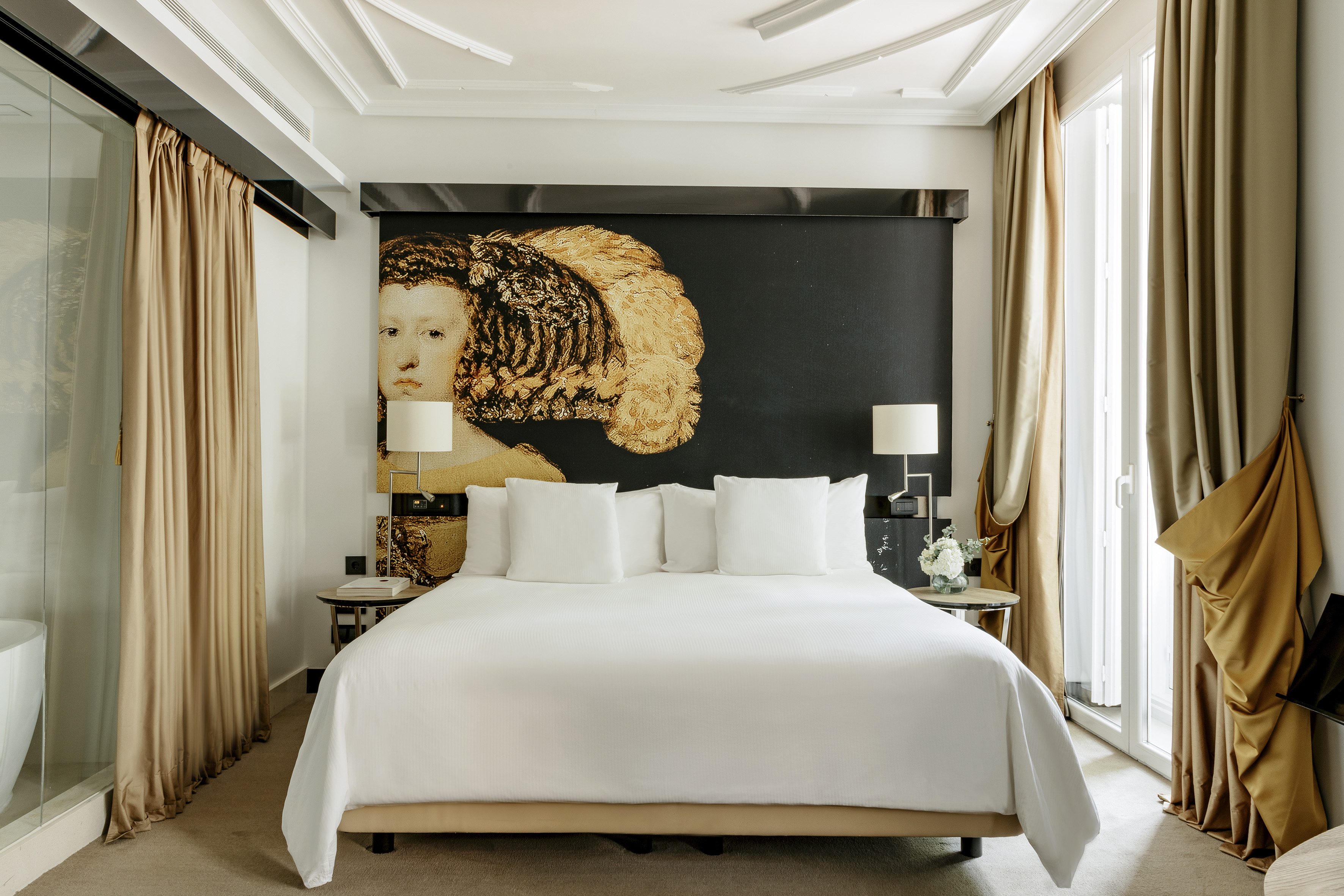 Luxury hotel room with white king bed and large golden portrait headboard.