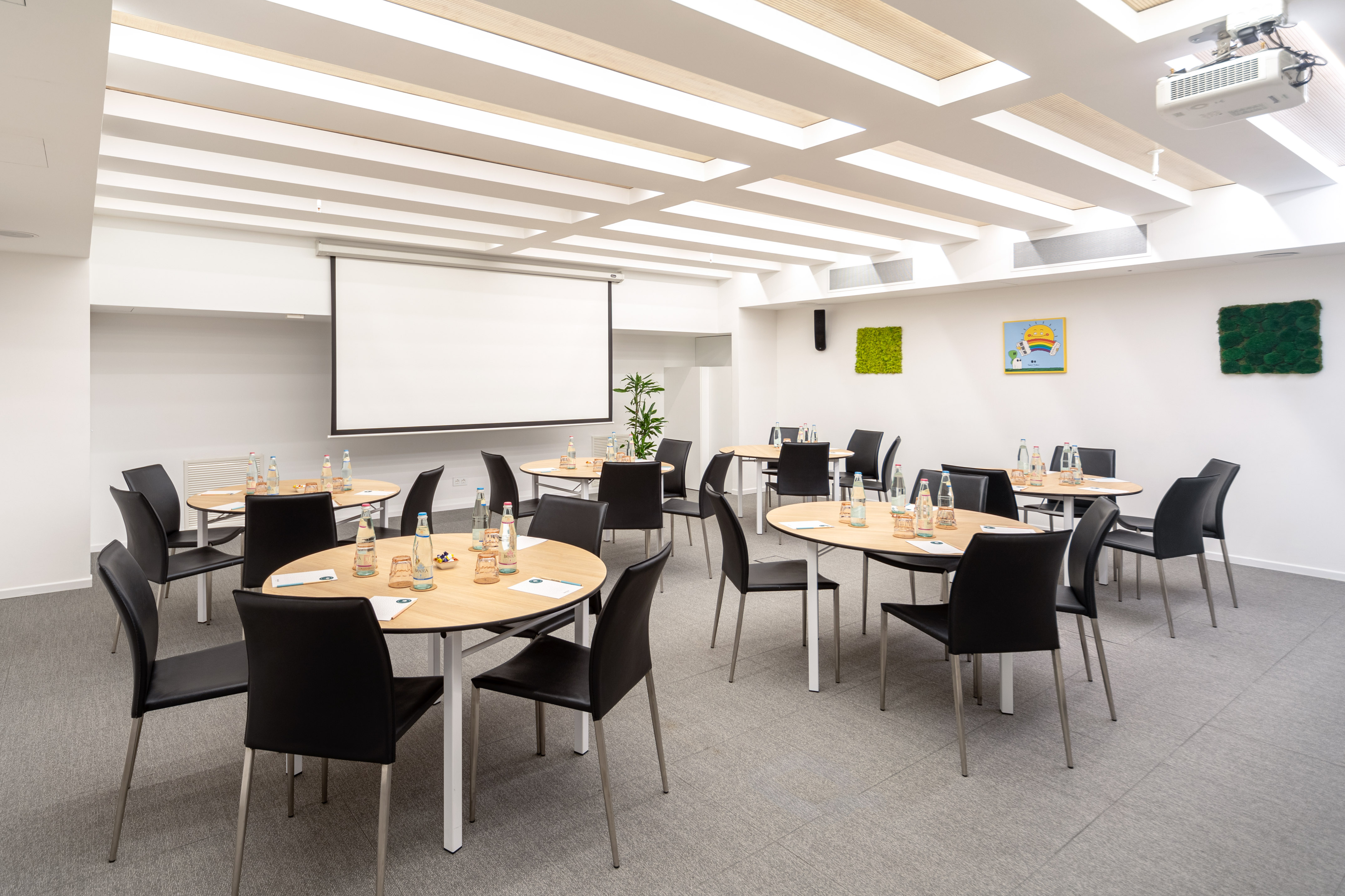 Conference room with round tables, projector, black chairs, and modern lighting.