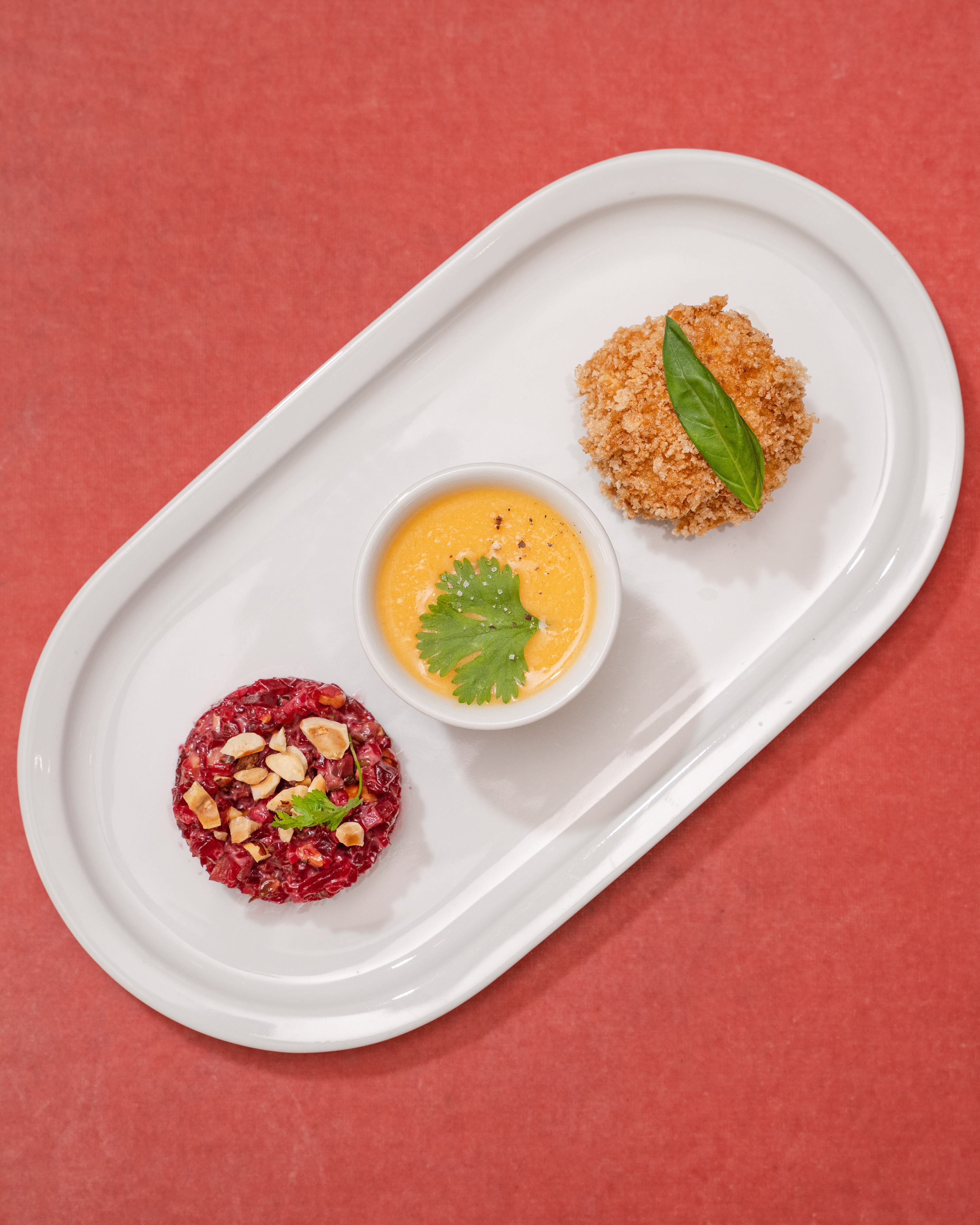 White plate with beetroot tartare, orange sauce, and crispy golden croquette.