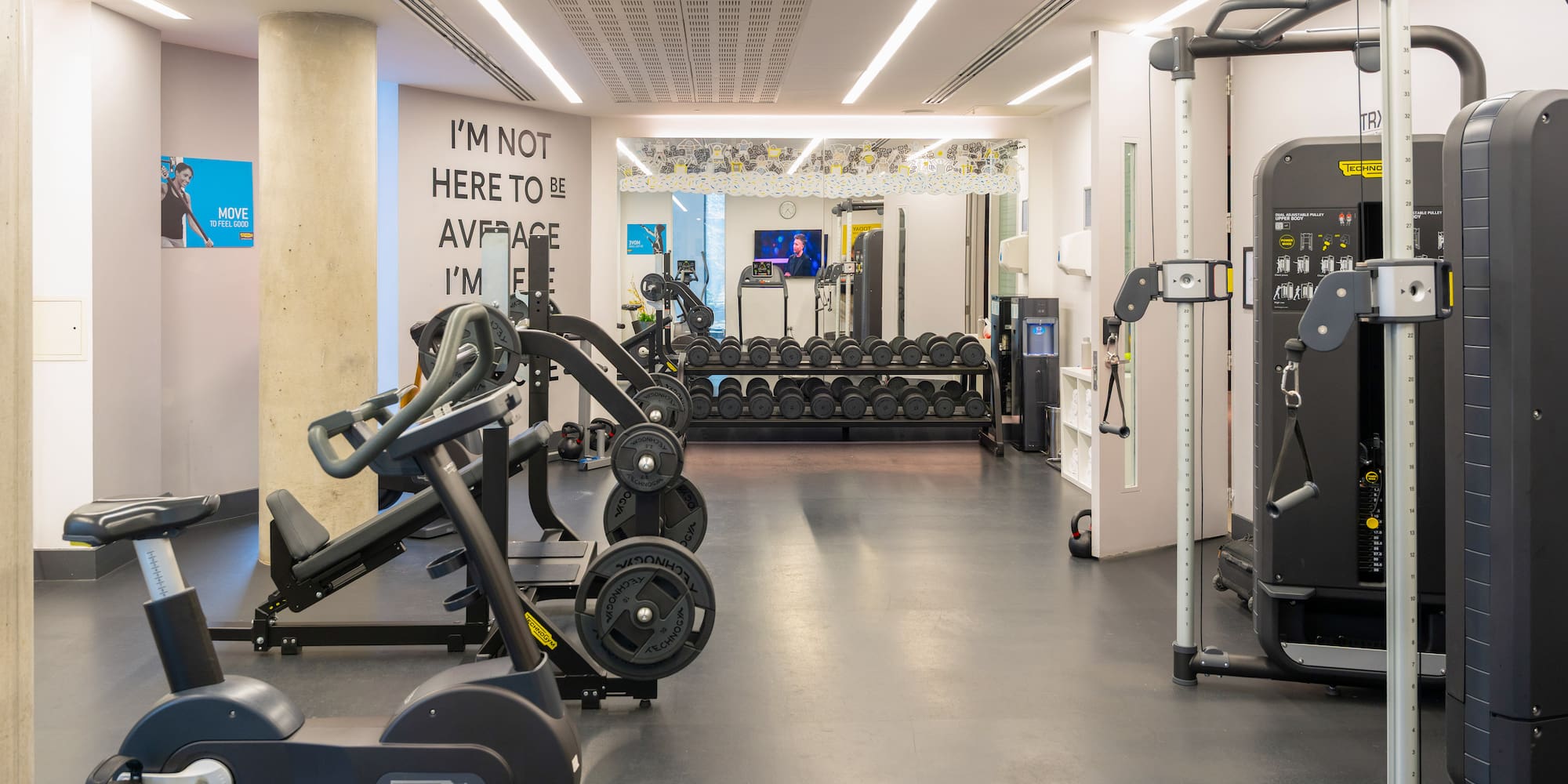Modern gym with Technogym bikes, weight machines, and dumbbell racks.