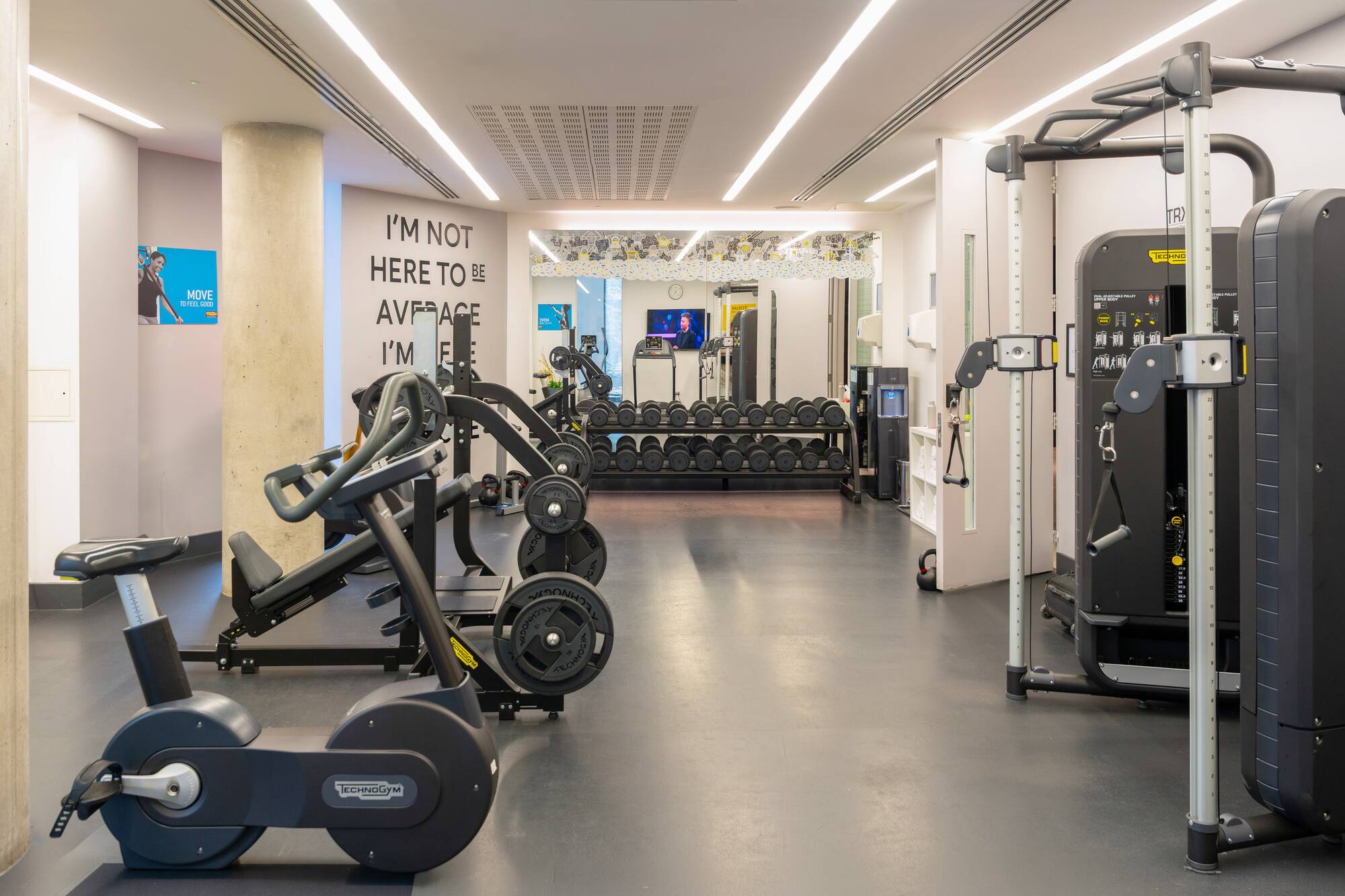 Modern gym with Technogym fitness equipment, exercise bikes, and dumbbell rack.