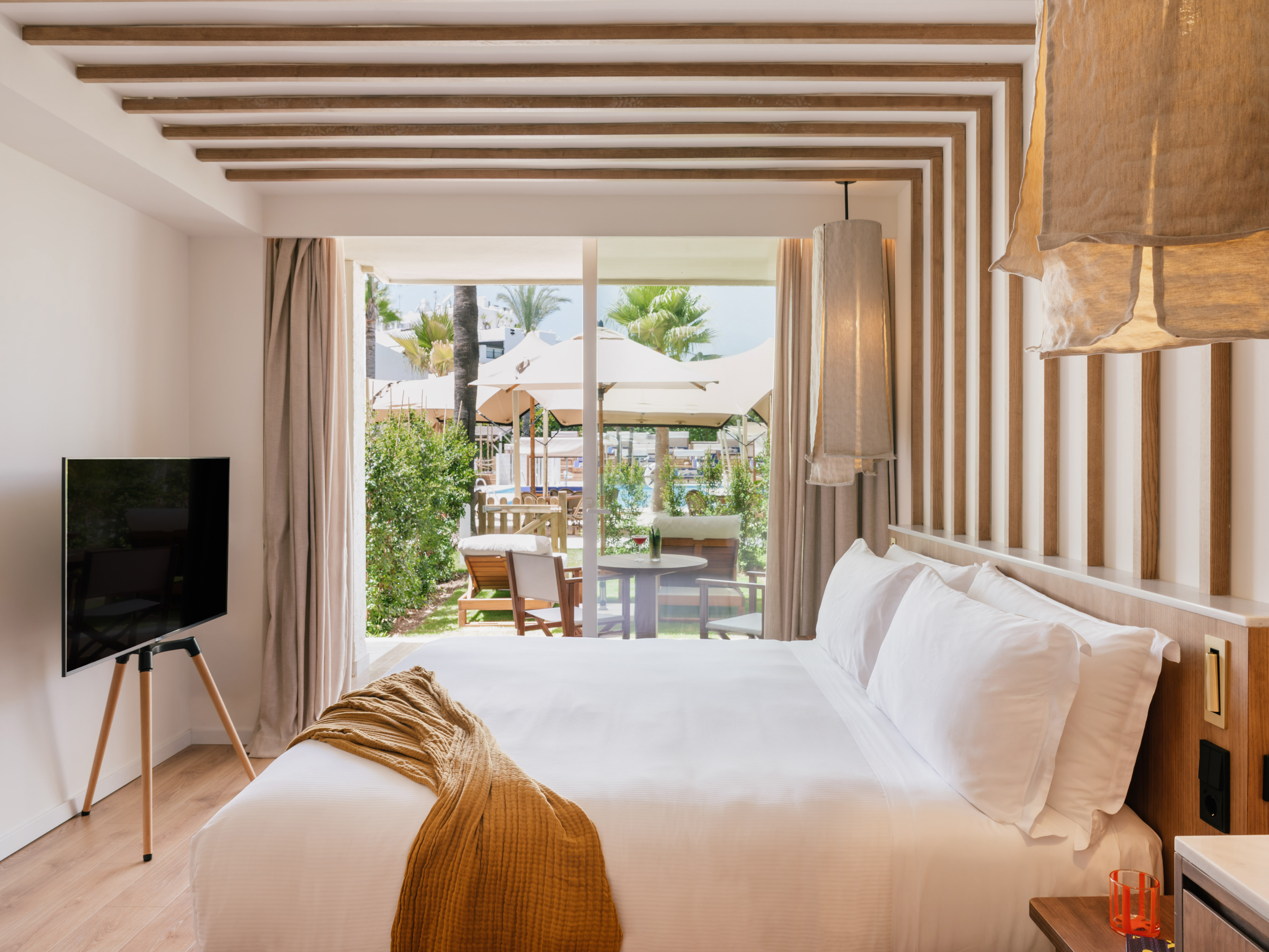 Modern resort bedroom with white bed, private patio, and tropical pool view.