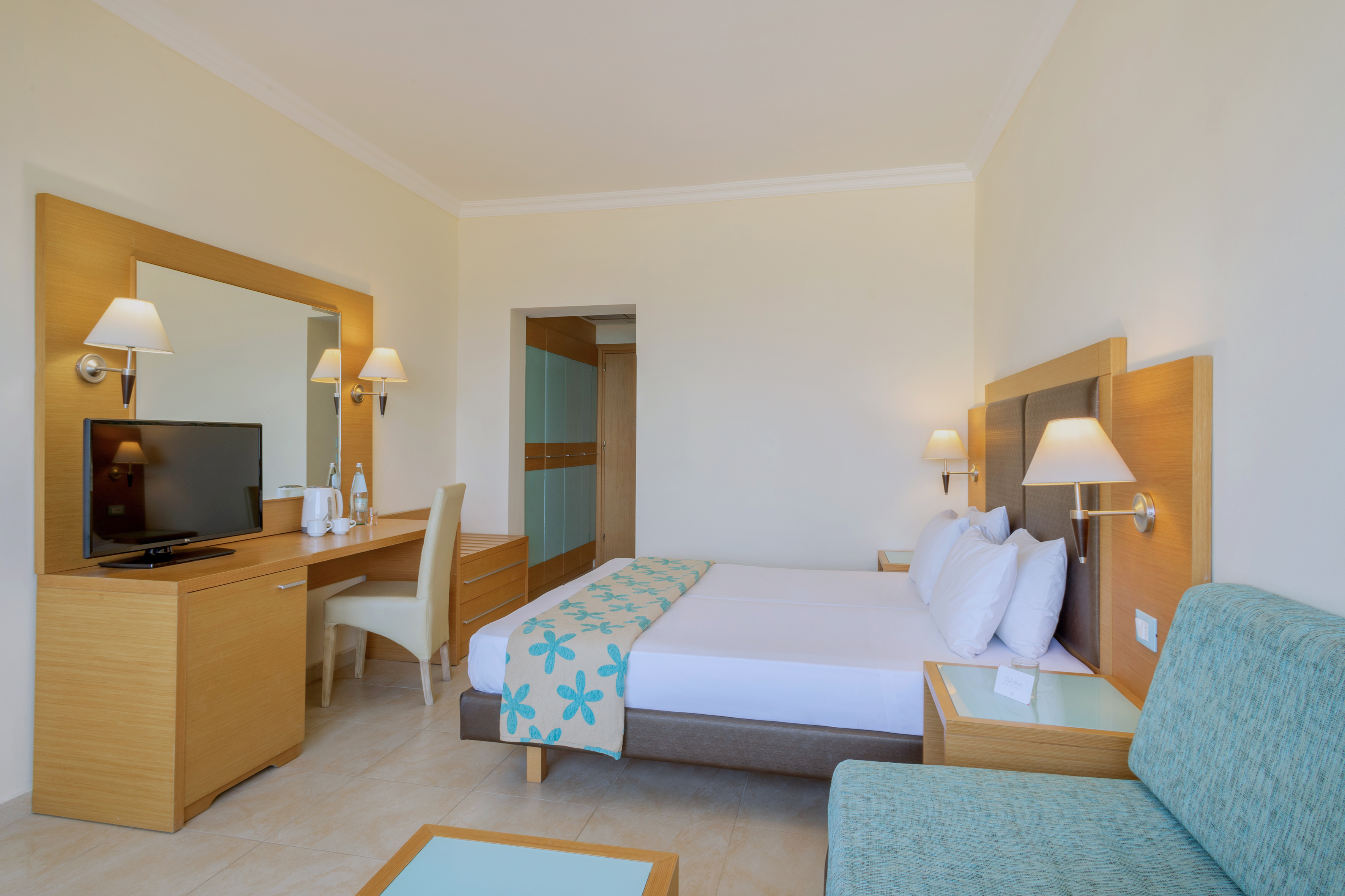 Modern hotel room with double bed, TV, desk, and blue sofa.