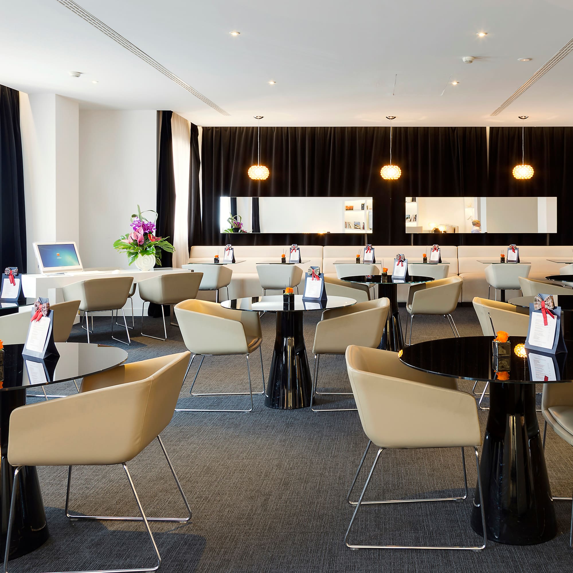Modern hotel lounge with black tables, beige chairs, and sleek decor.