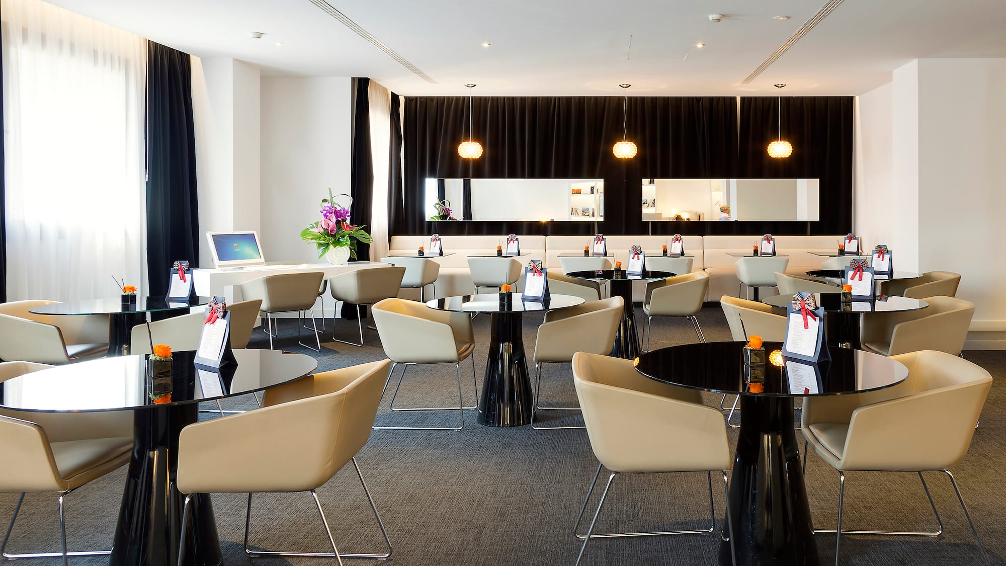 Modern hotel lounge with black tables, beige chairs, and sleek decor.