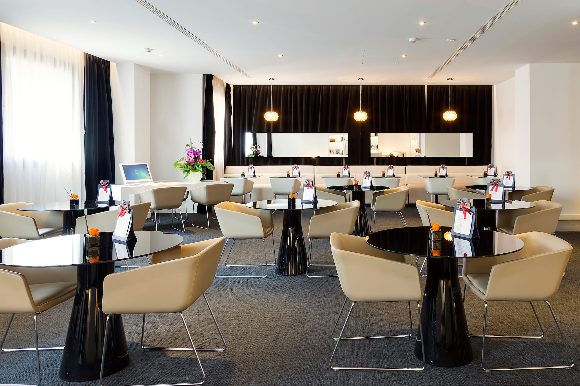 Modern hotel lounge with black tables, beige chairs, and sleek decor.