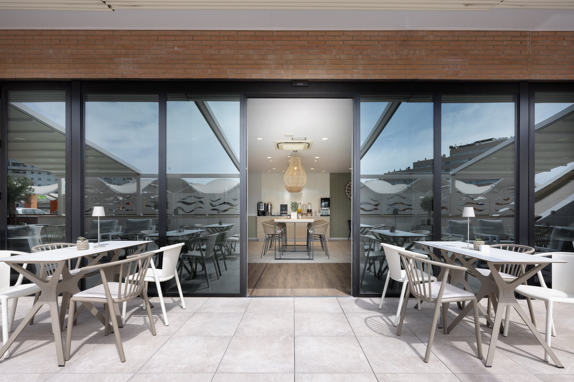 Modern outdoor dining patio with tables, chairs, and glass doors to indoor cafe.
