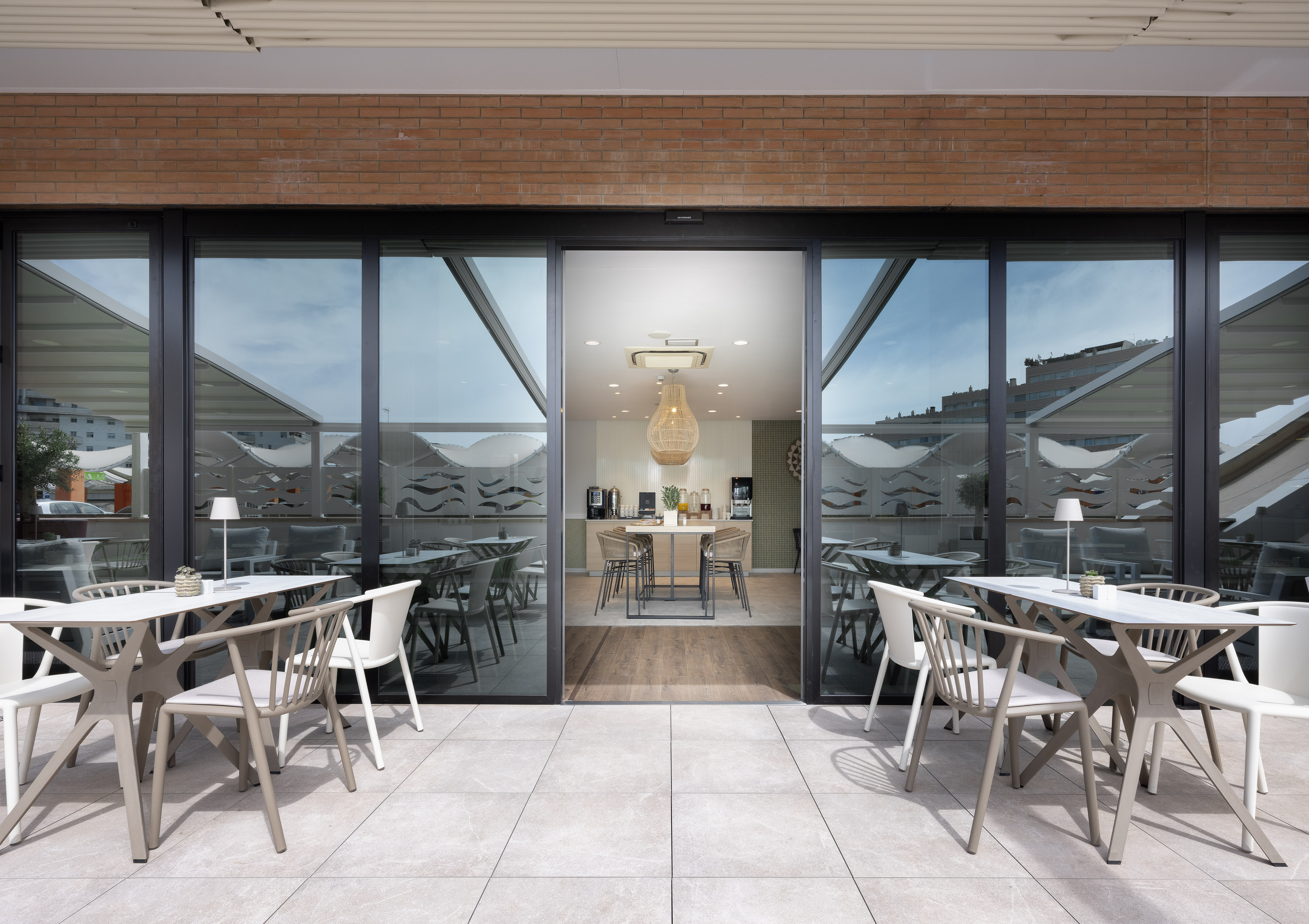 Modern outdoor dining patio with tables, chairs, and glass doors to indoor cafe.