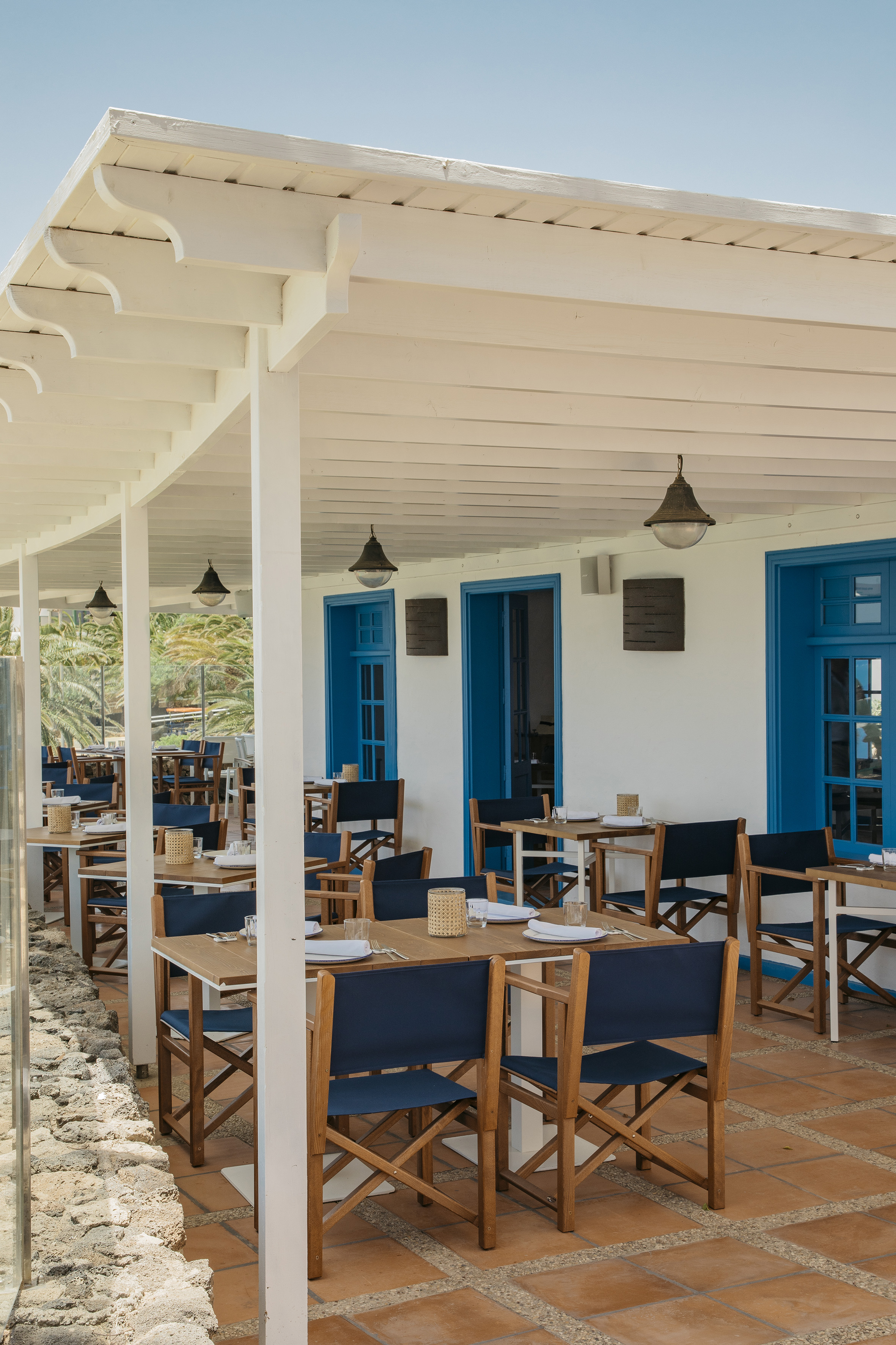 Outdoor Mediterranean restaurant patio with blue doors and wooden tables.