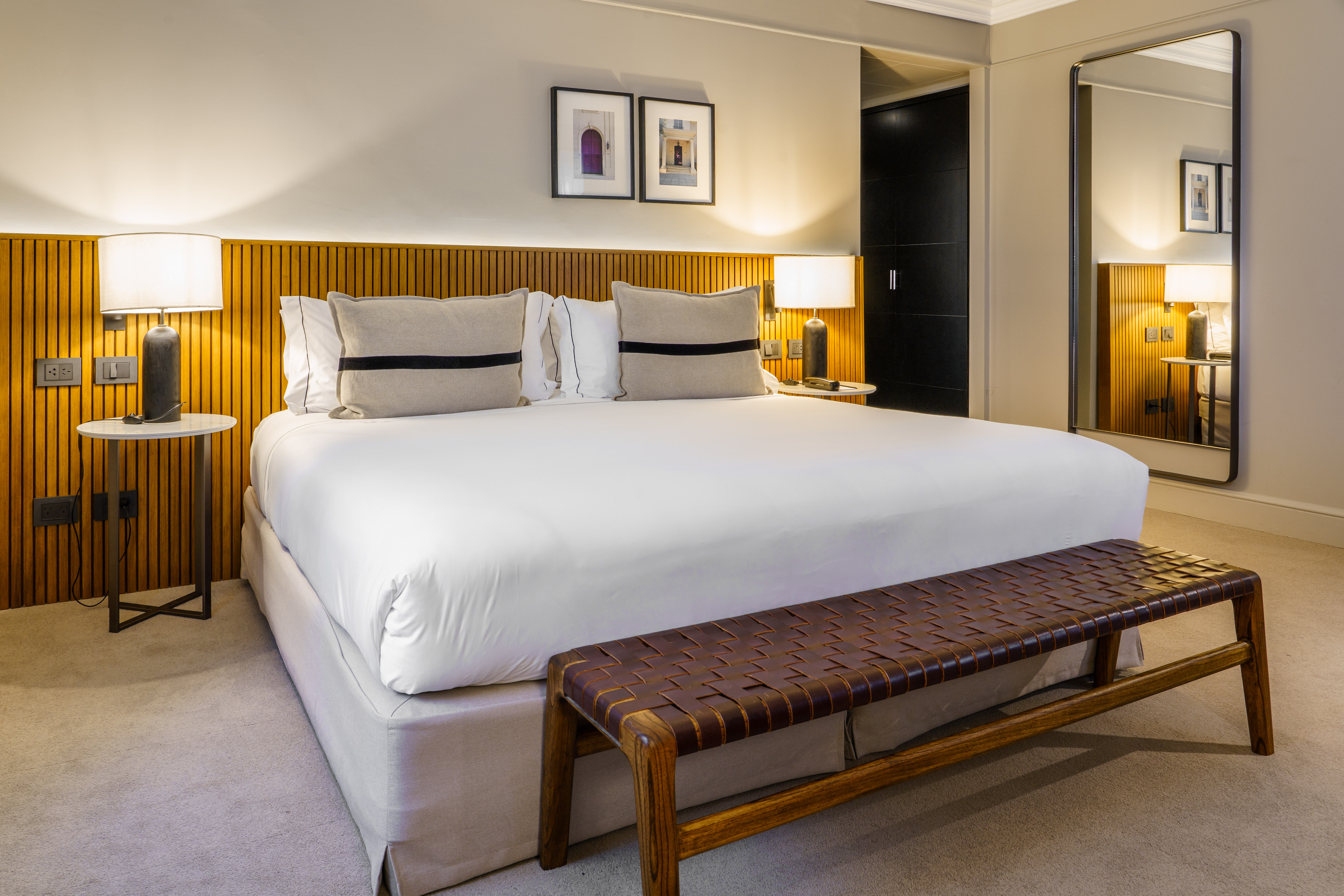 Modern hotel bedroom, king bed, wood headboard, bedside lamps, woven bench.