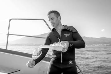 a man in a wet suit pouring wine into a glass on a boat