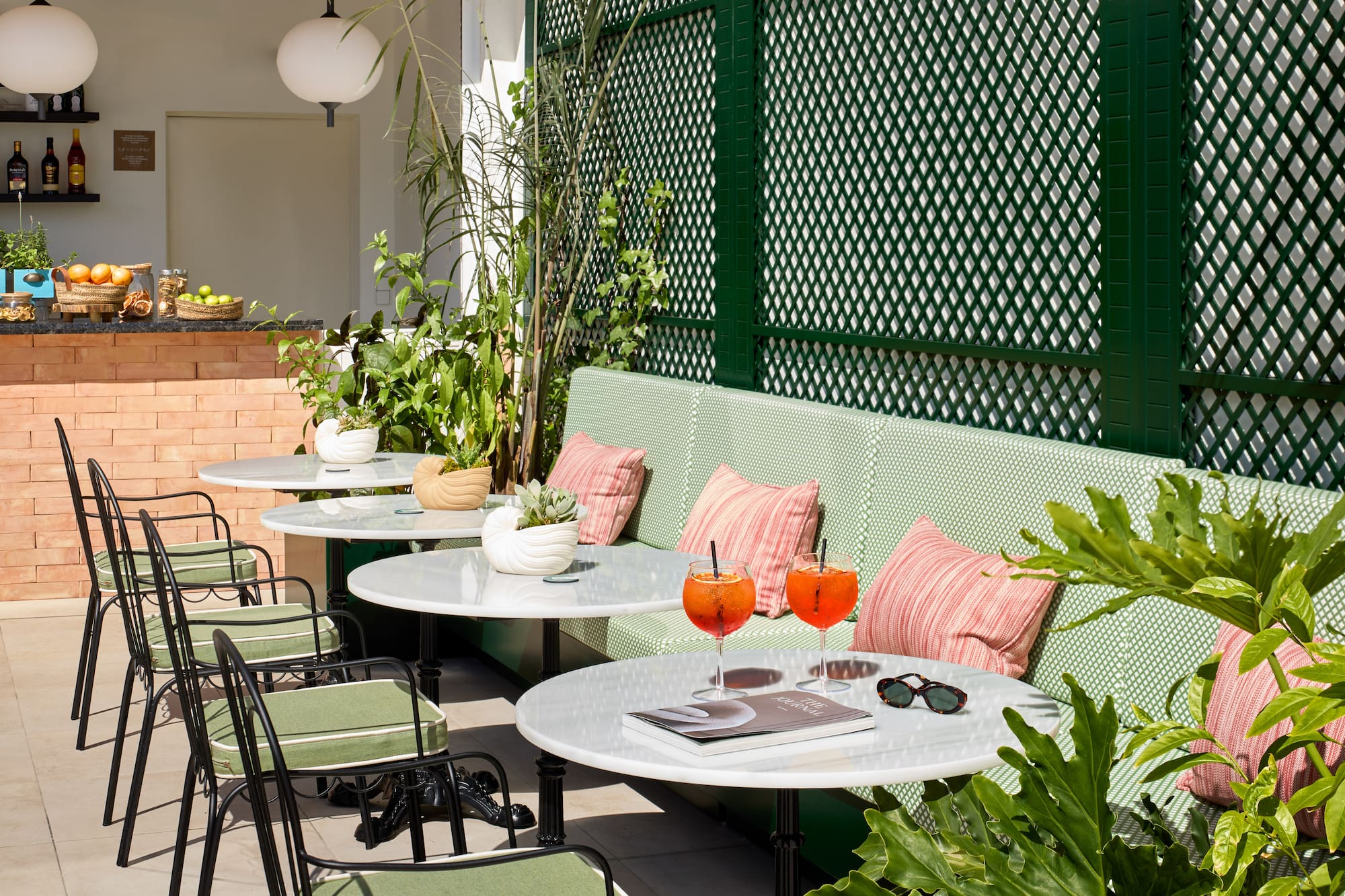 Outdoor patio with green lattice, marble tables, cocktails, and lush plants.