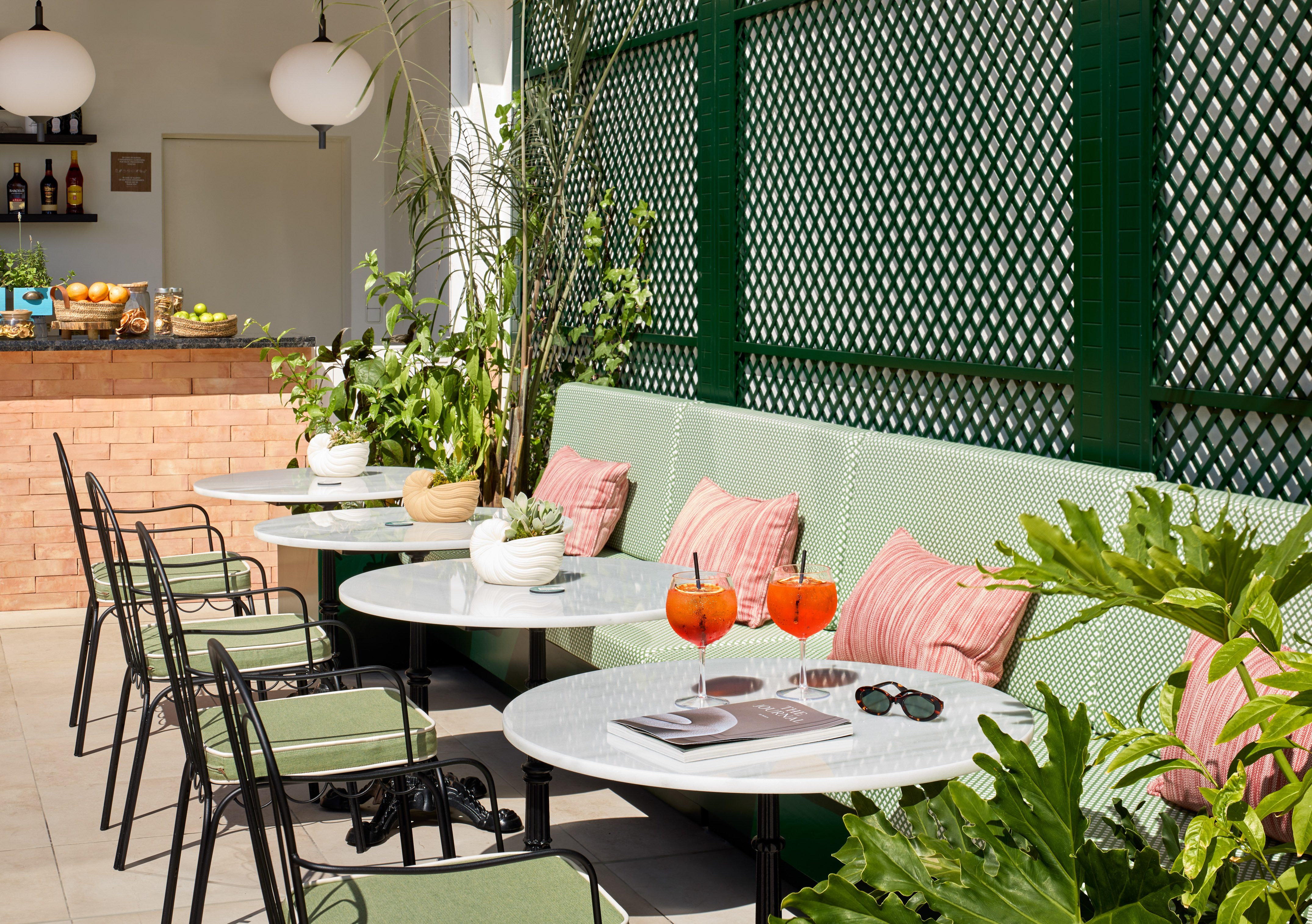 Outdoor patio with green lattice, marble tables, cocktails, and lush plants.