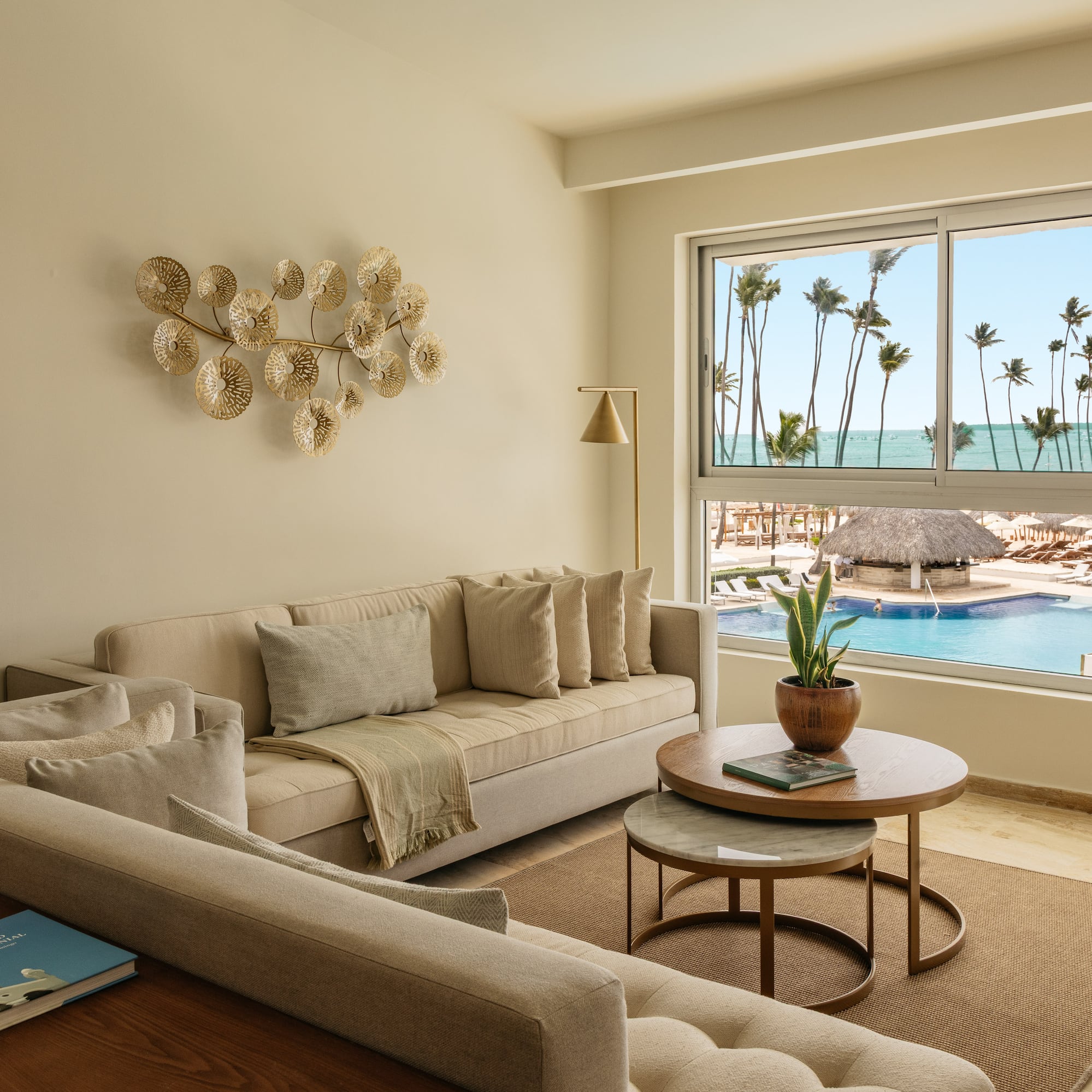 Modern living room overlooking resort pool, ocean, and palm trees.