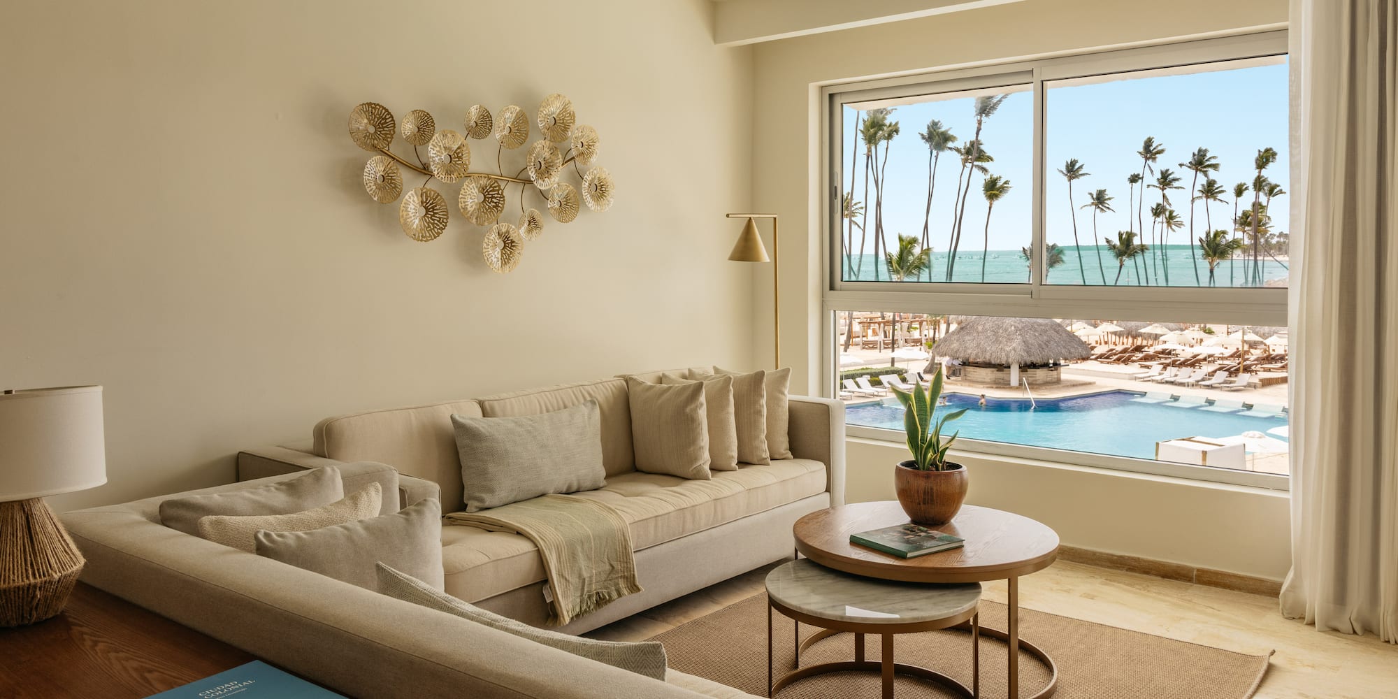 Modern living room overlooking resort pool, ocean, and palm trees.