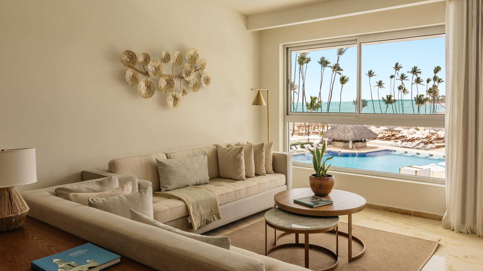 Modern living room overlooking resort pool, ocean, and palm trees.