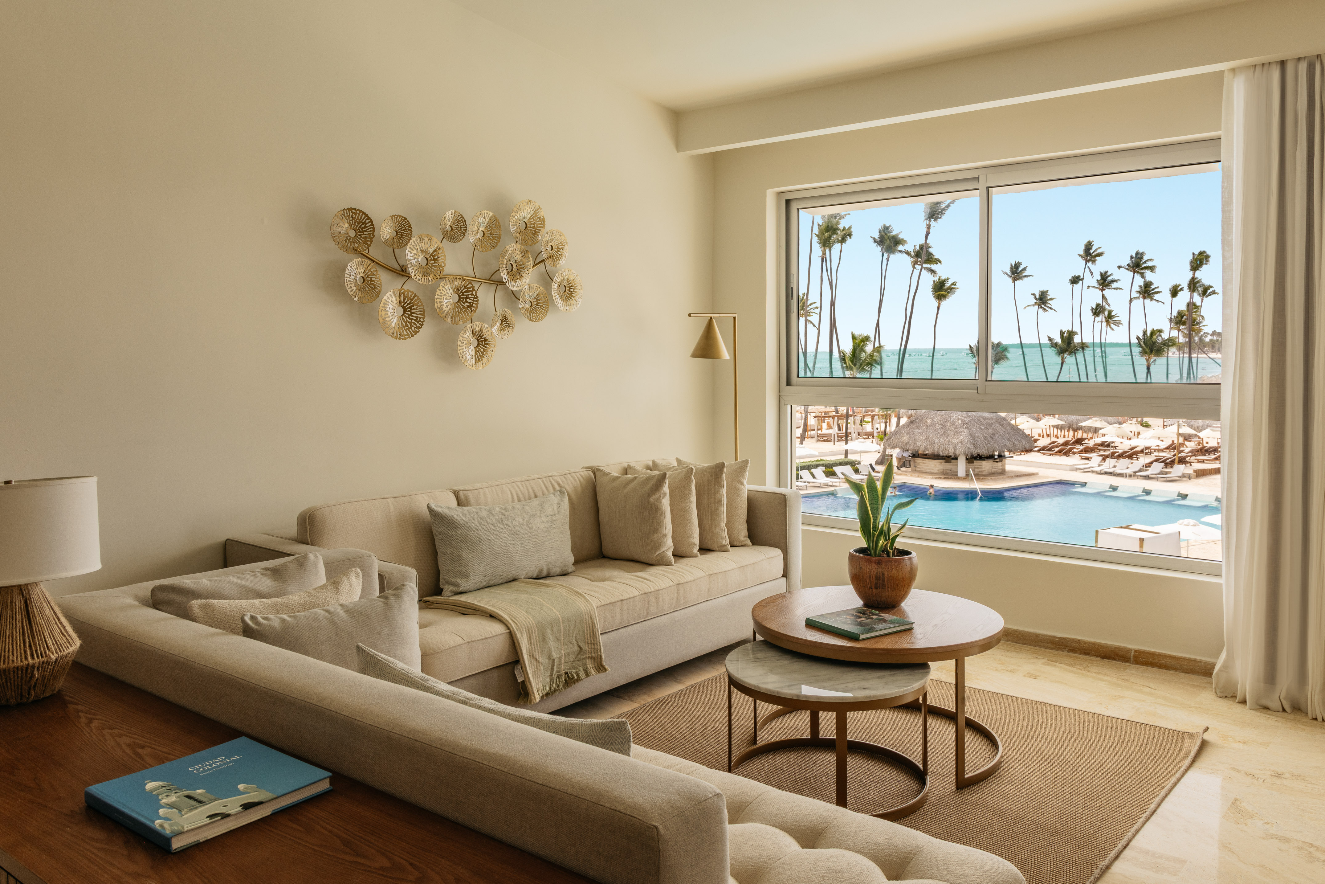 Modern living room overlooking resort pool, ocean, and palm trees.
