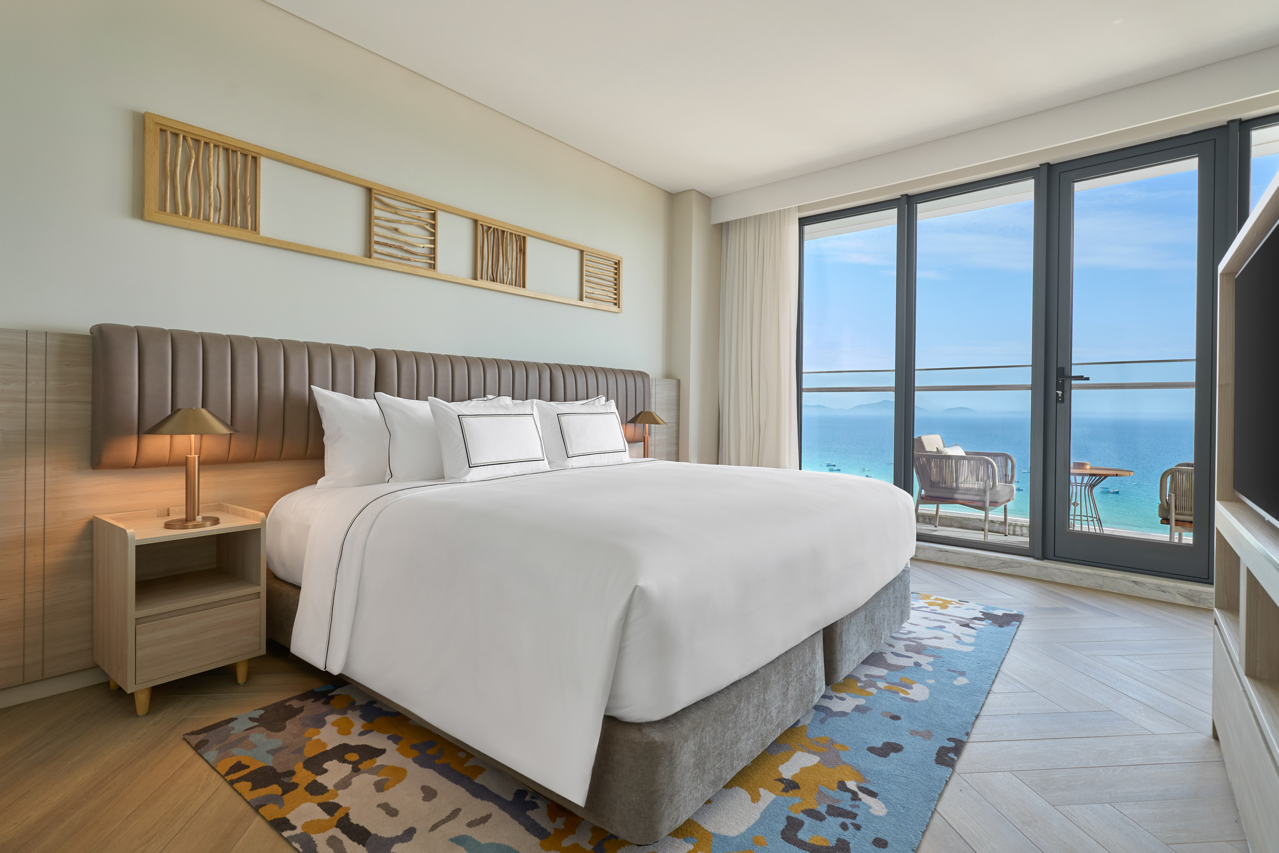 Luxury hotel bedroom with king bed and panoramic ocean view balcony.