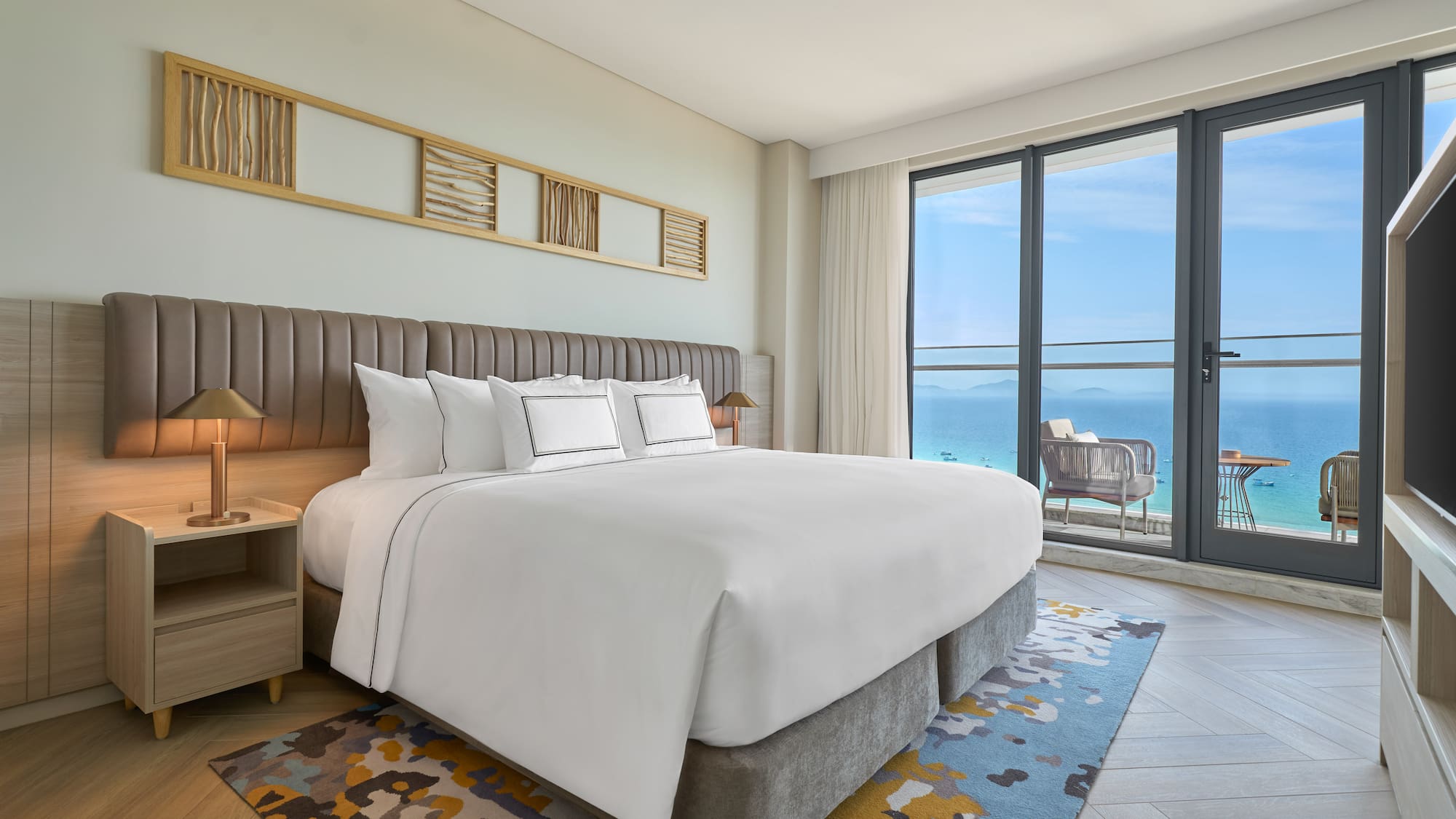 Luxury hotel bedroom with king bed and panoramic ocean view balcony.