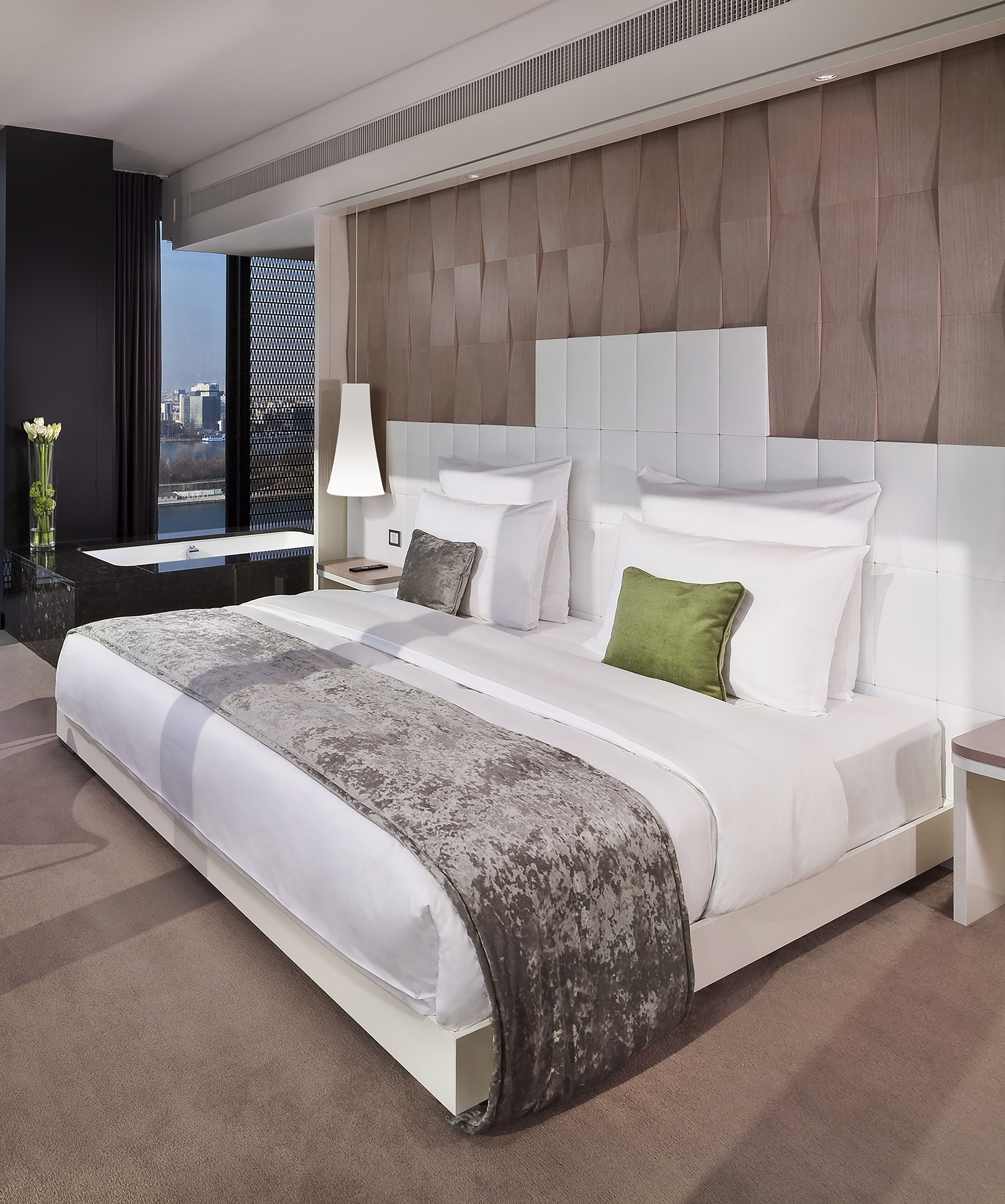 Luxury hotel suite with modern king bed, city view, and elegant bathtub.