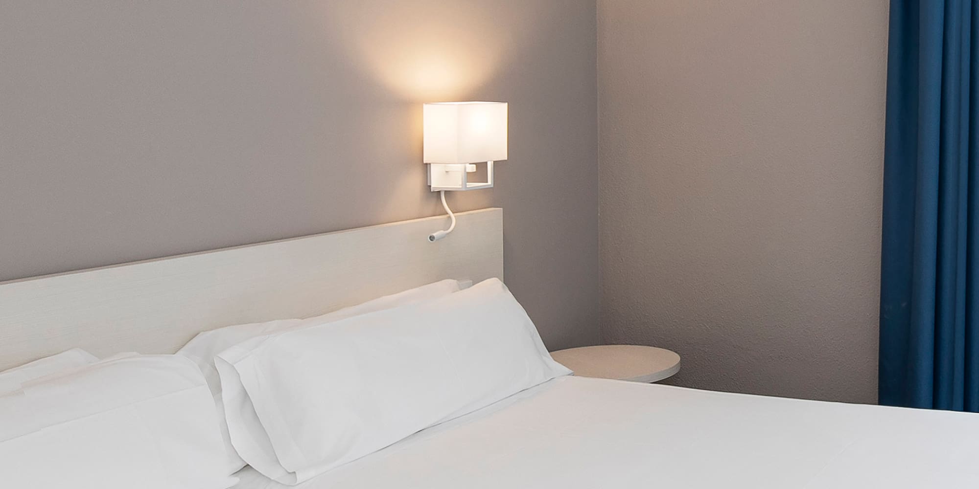 a bed with white sheets and a lamp on the wall
