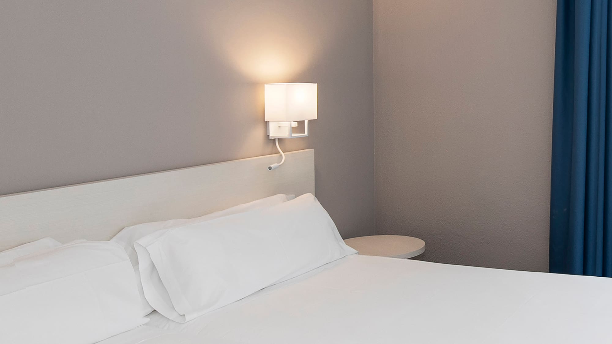 a bed with white sheets and a lamp on the wall