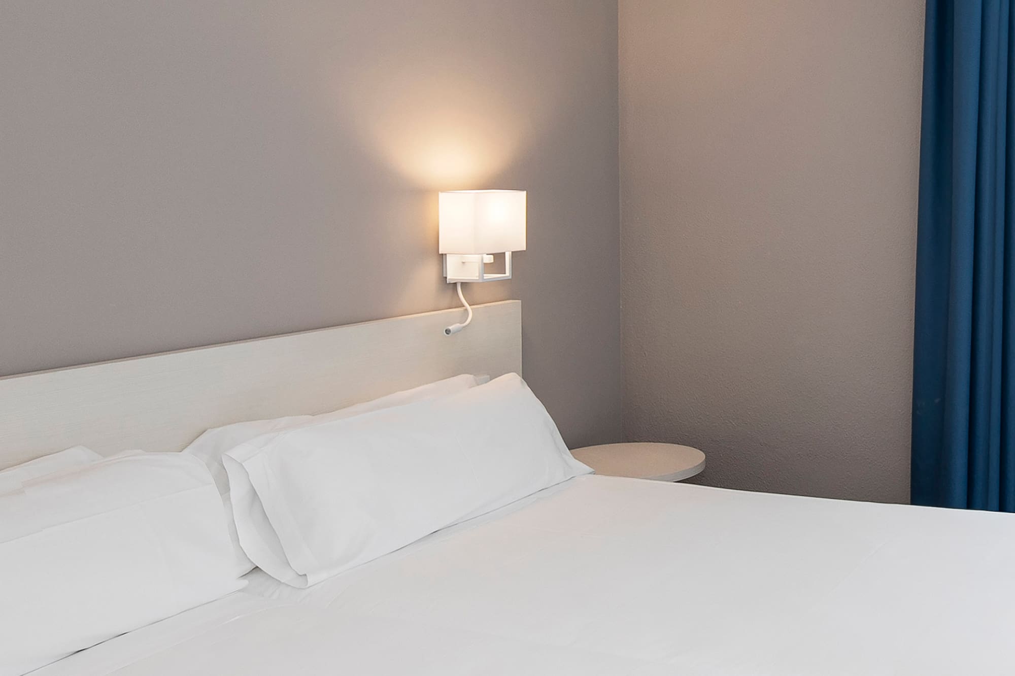 a bed with white sheets and a lamp on the wall