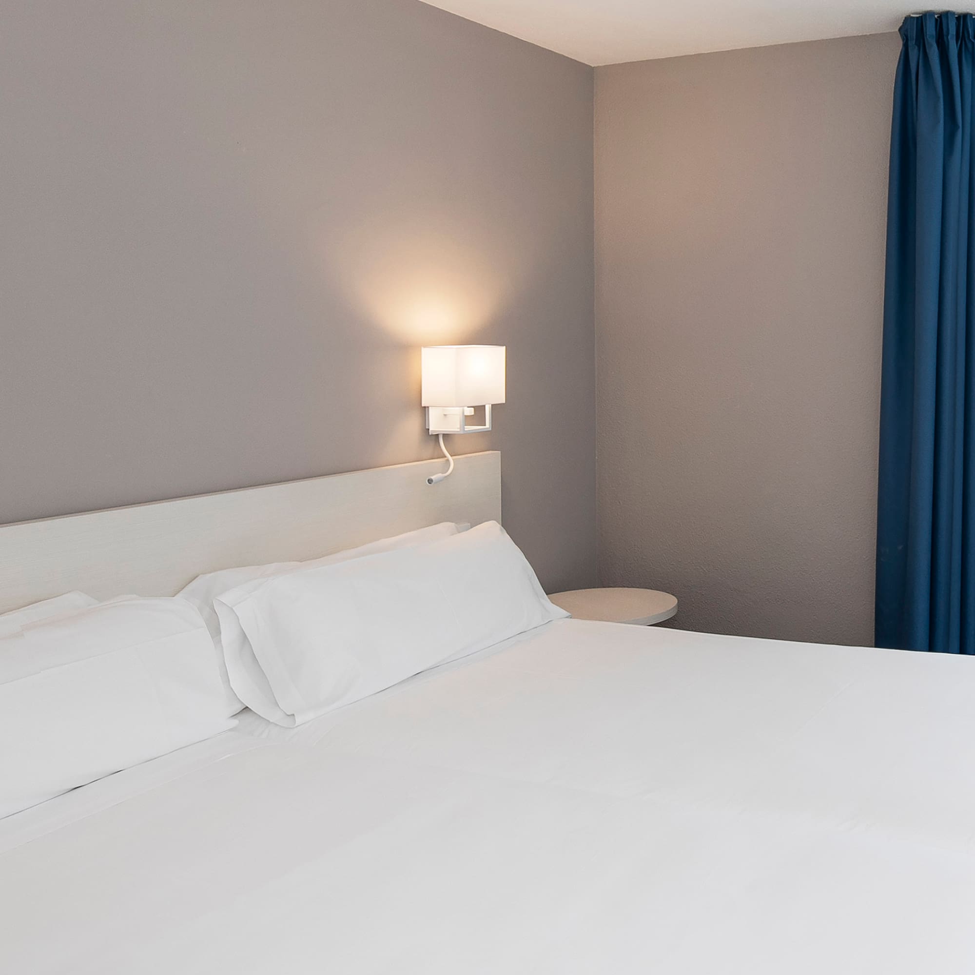 a bed with white sheets and a lamp on the wall