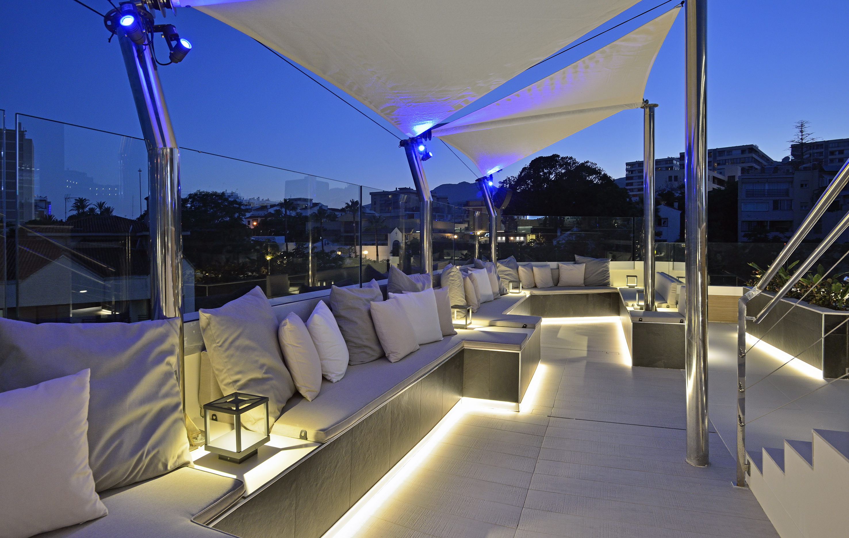 Evening rooftop lounge with illuminated modern seating and white shade sails.