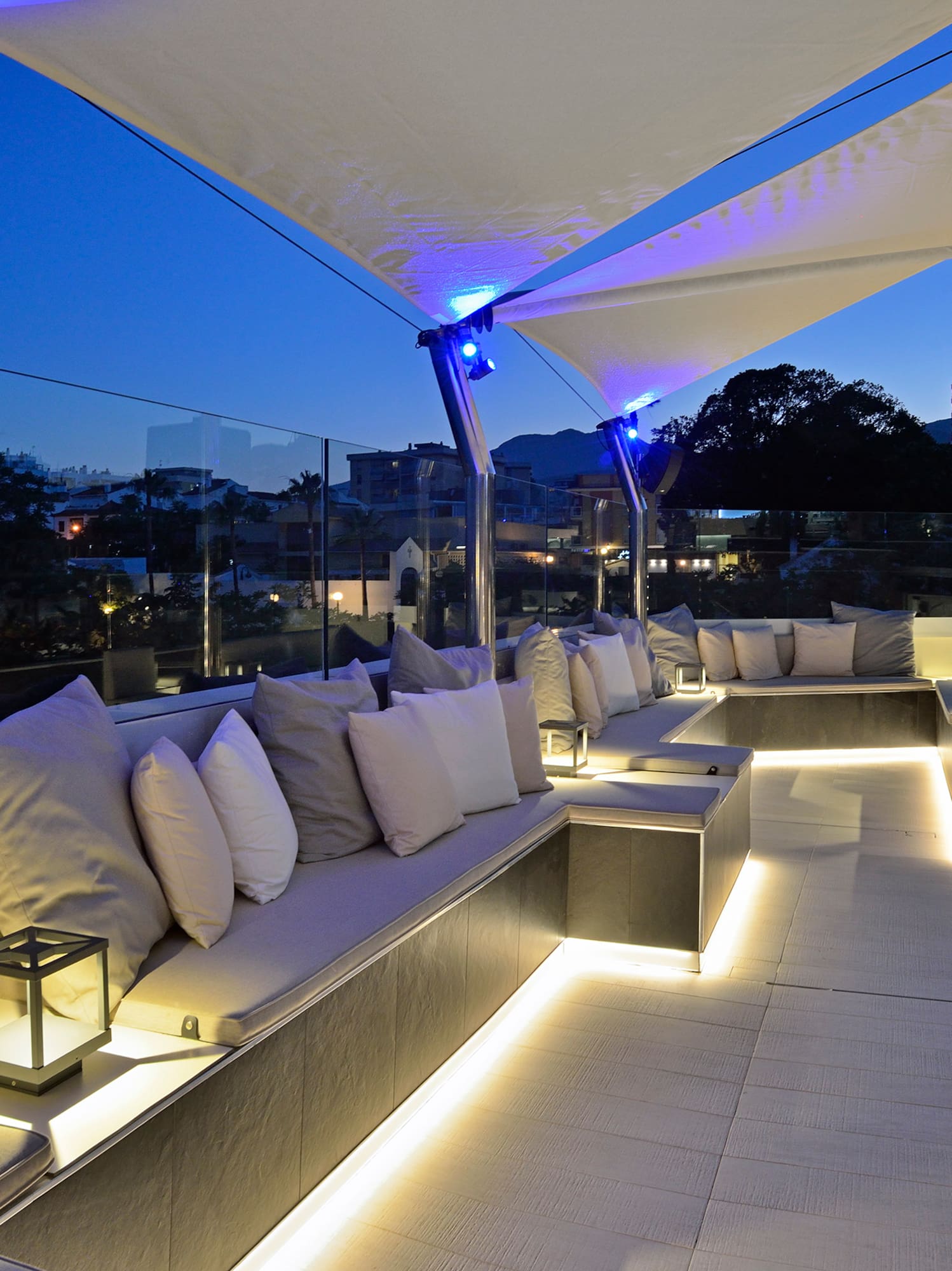 Evening rooftop lounge with illuminated modern seating and white shade sails.
