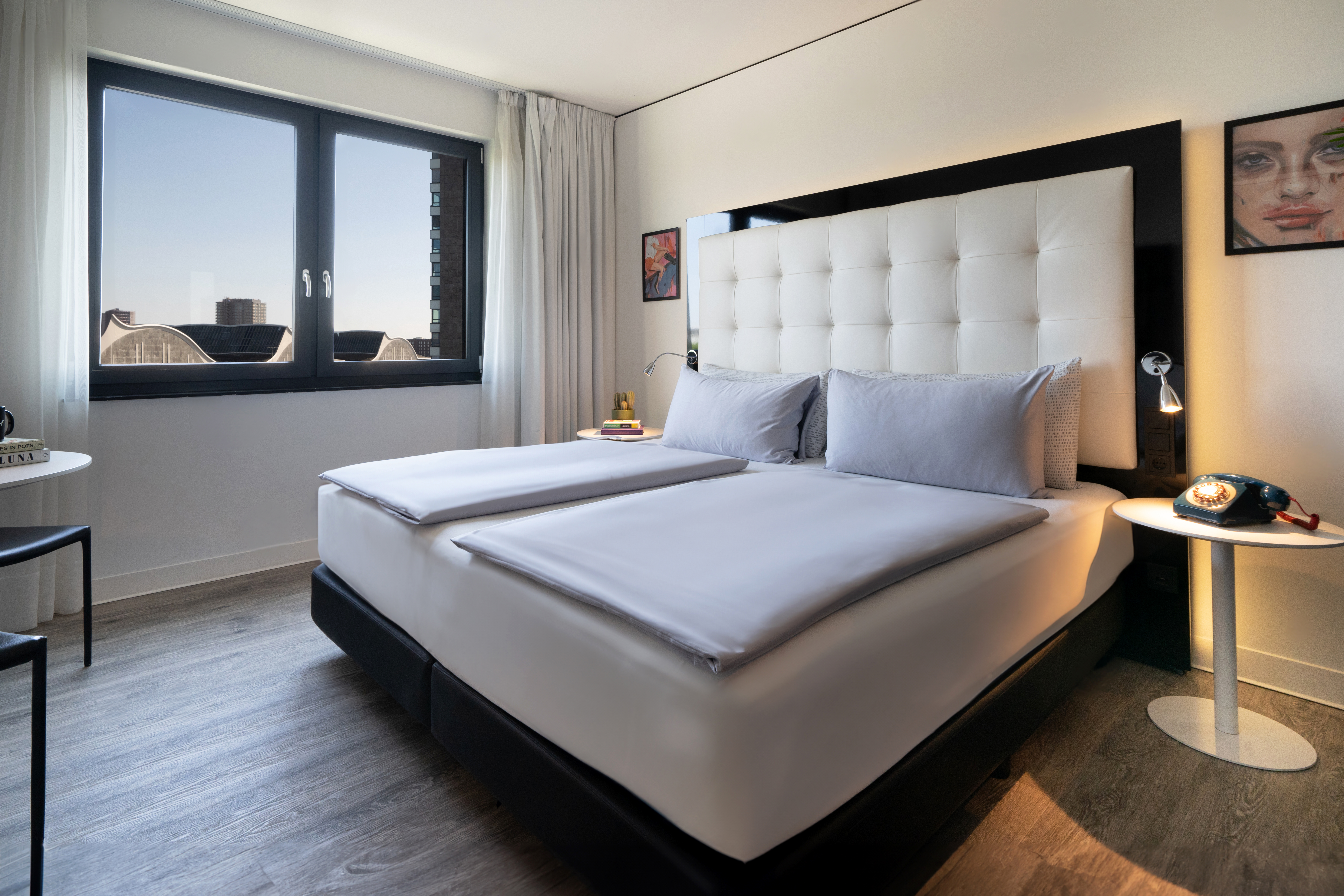 Contemporary hotel room with large bed, grey bedding, and city view window.