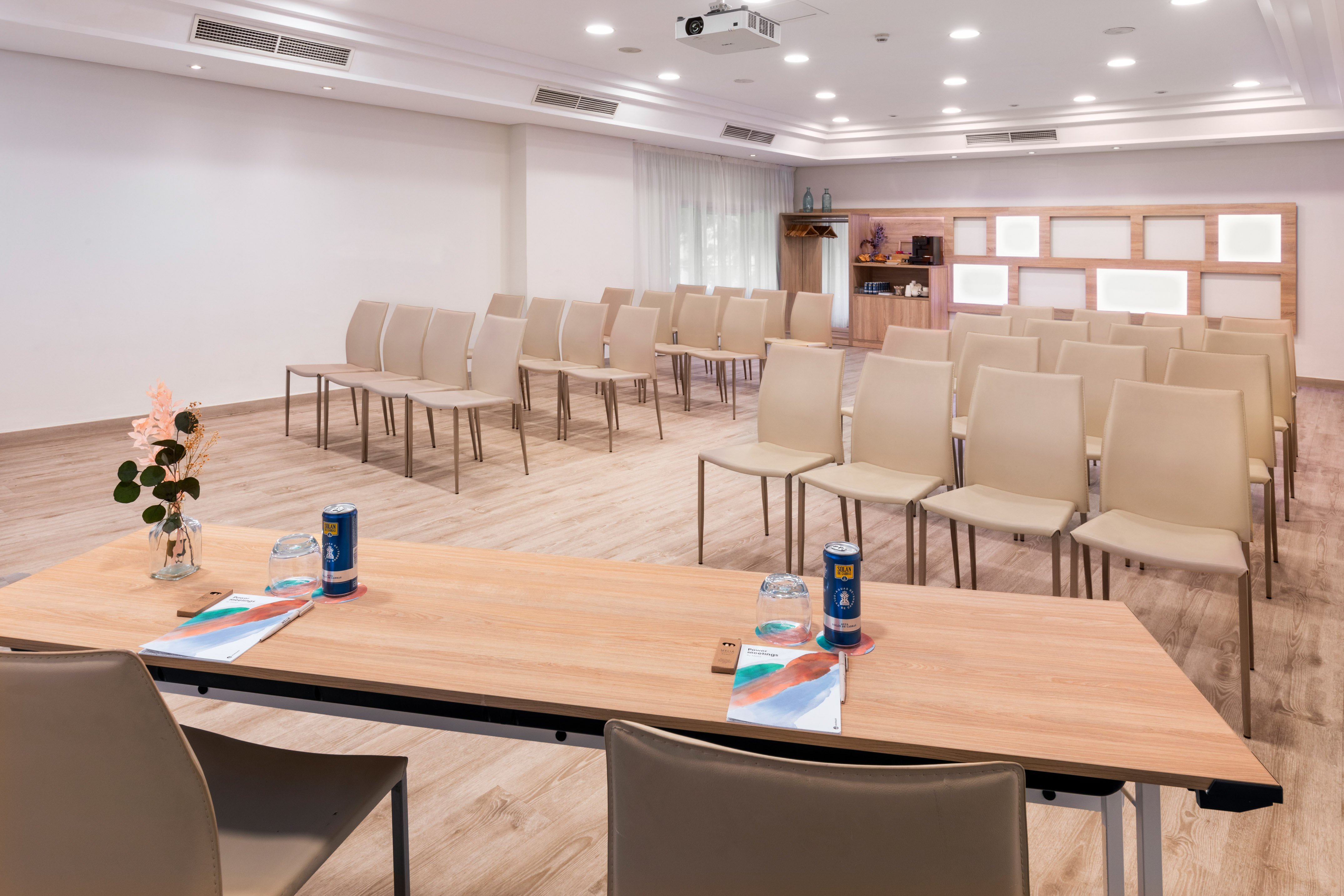 Modern conference room with rows of chairs, projector, and refreshment station.
