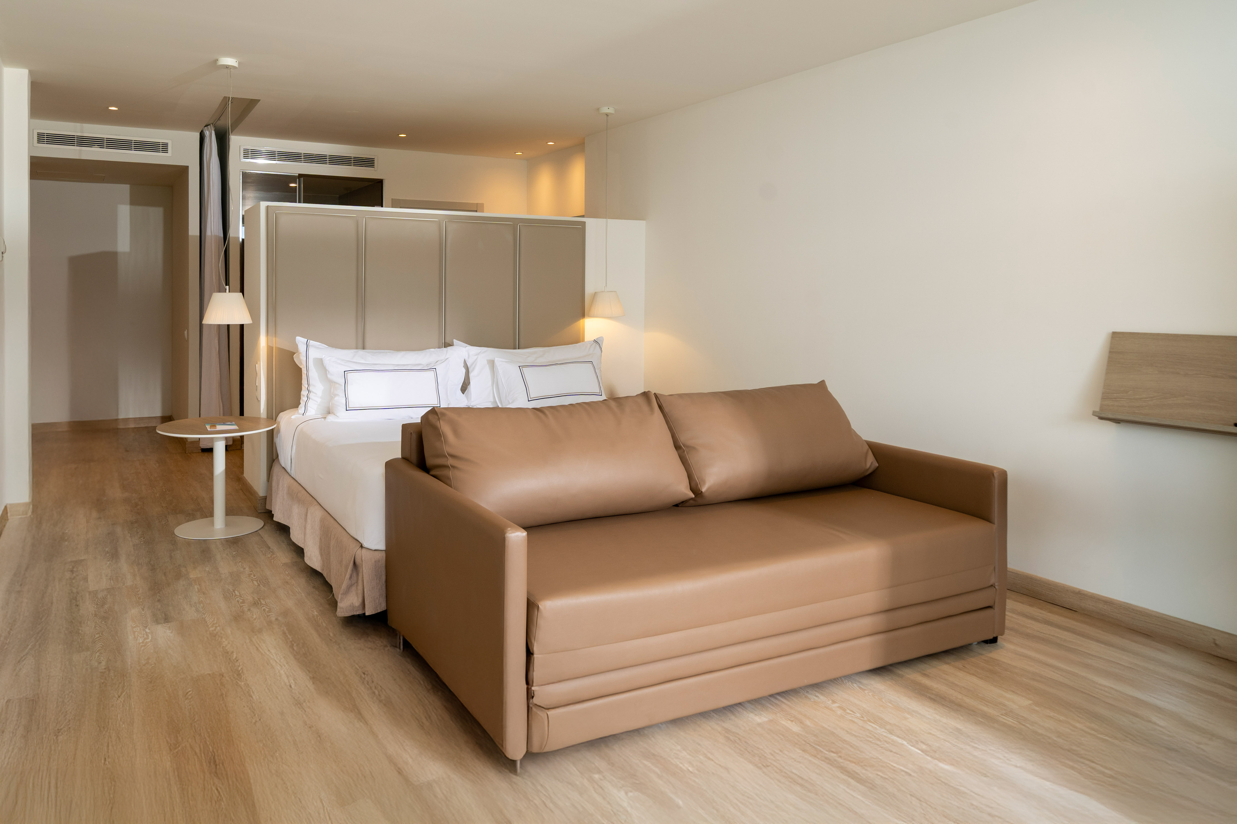 Modern hotel suite with king bed and convertible brown sofa bed.