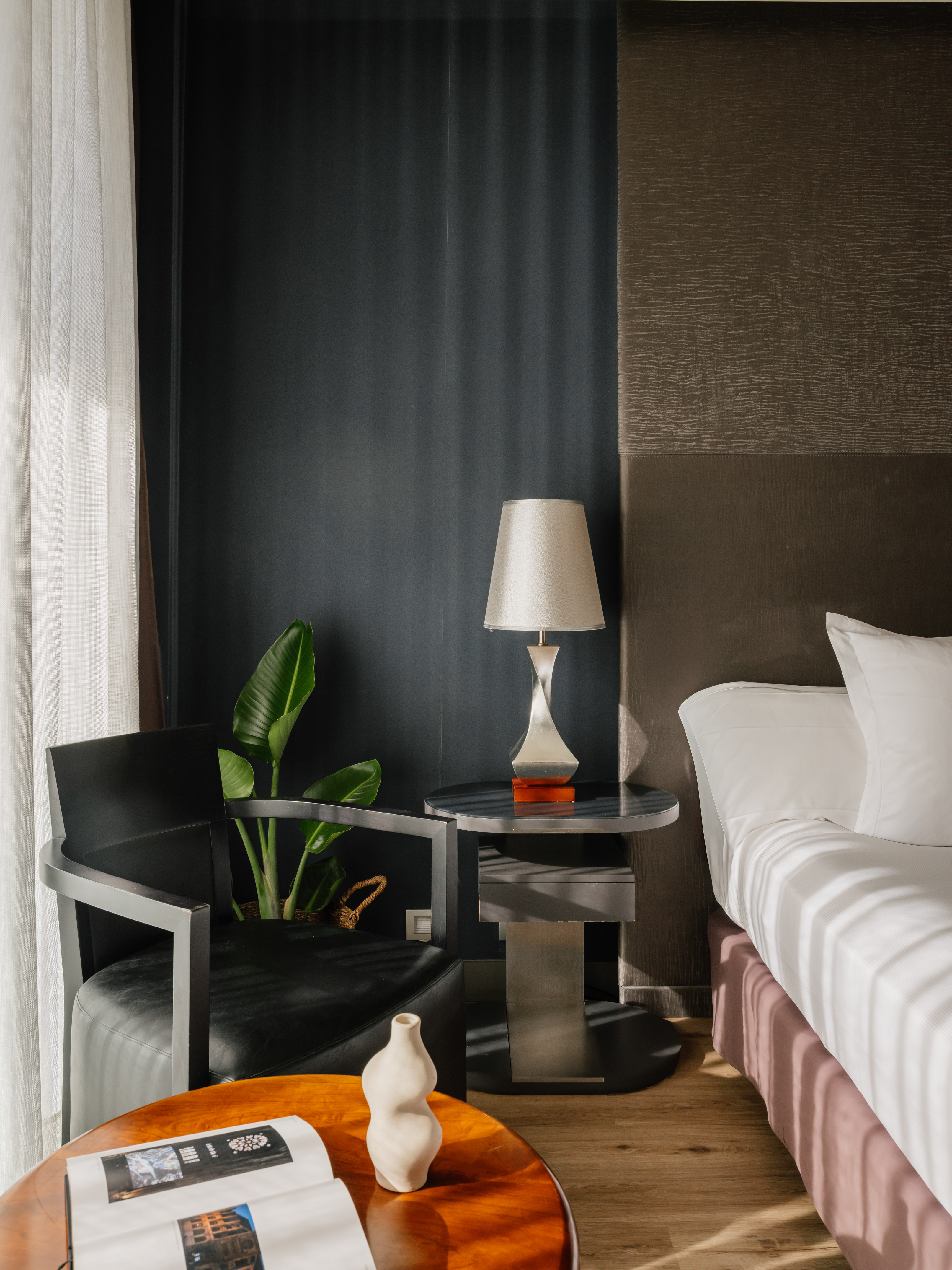 Stylish hotel bedroom featuring white bed, dark walls, modern chair, and lamp.