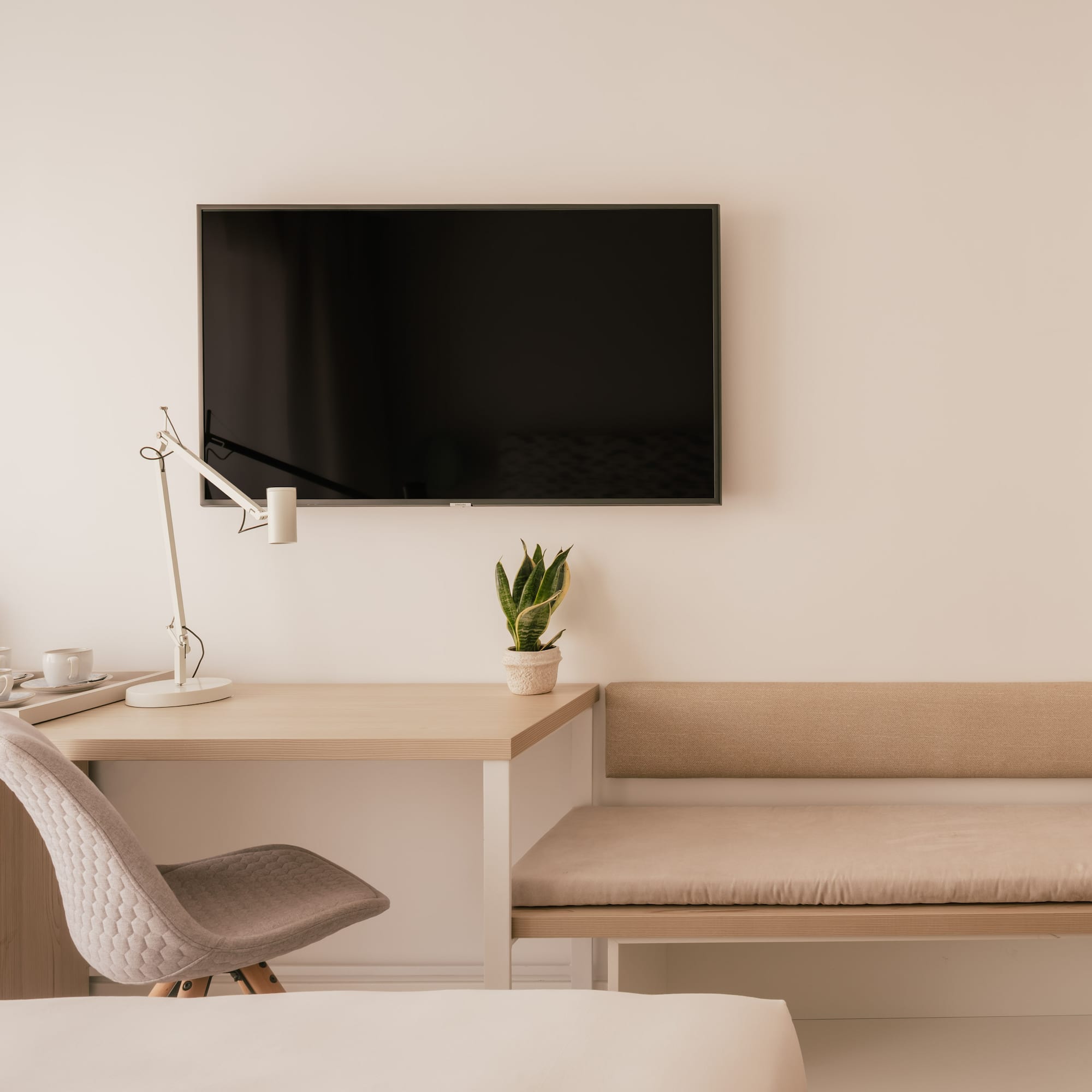 Modern hotel room with desk, wall TV, coffee station, and bench seating.