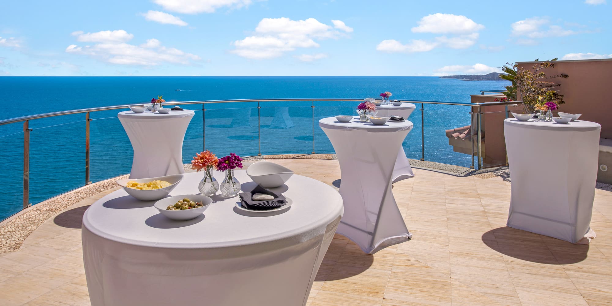 White highboy tables on an ocean-view terrace, set for a cocktail event.