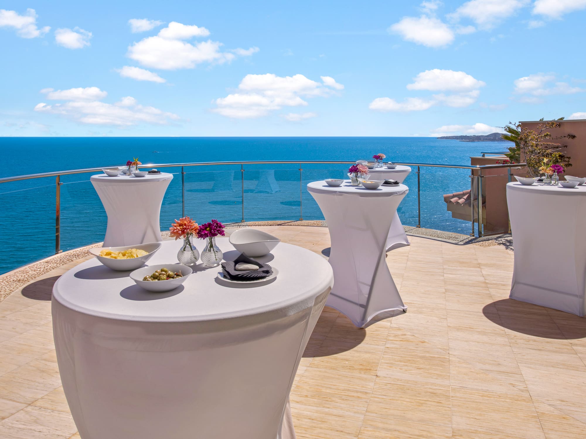 Outdoor terrace with white cocktail tables, snacks, and ocean view.