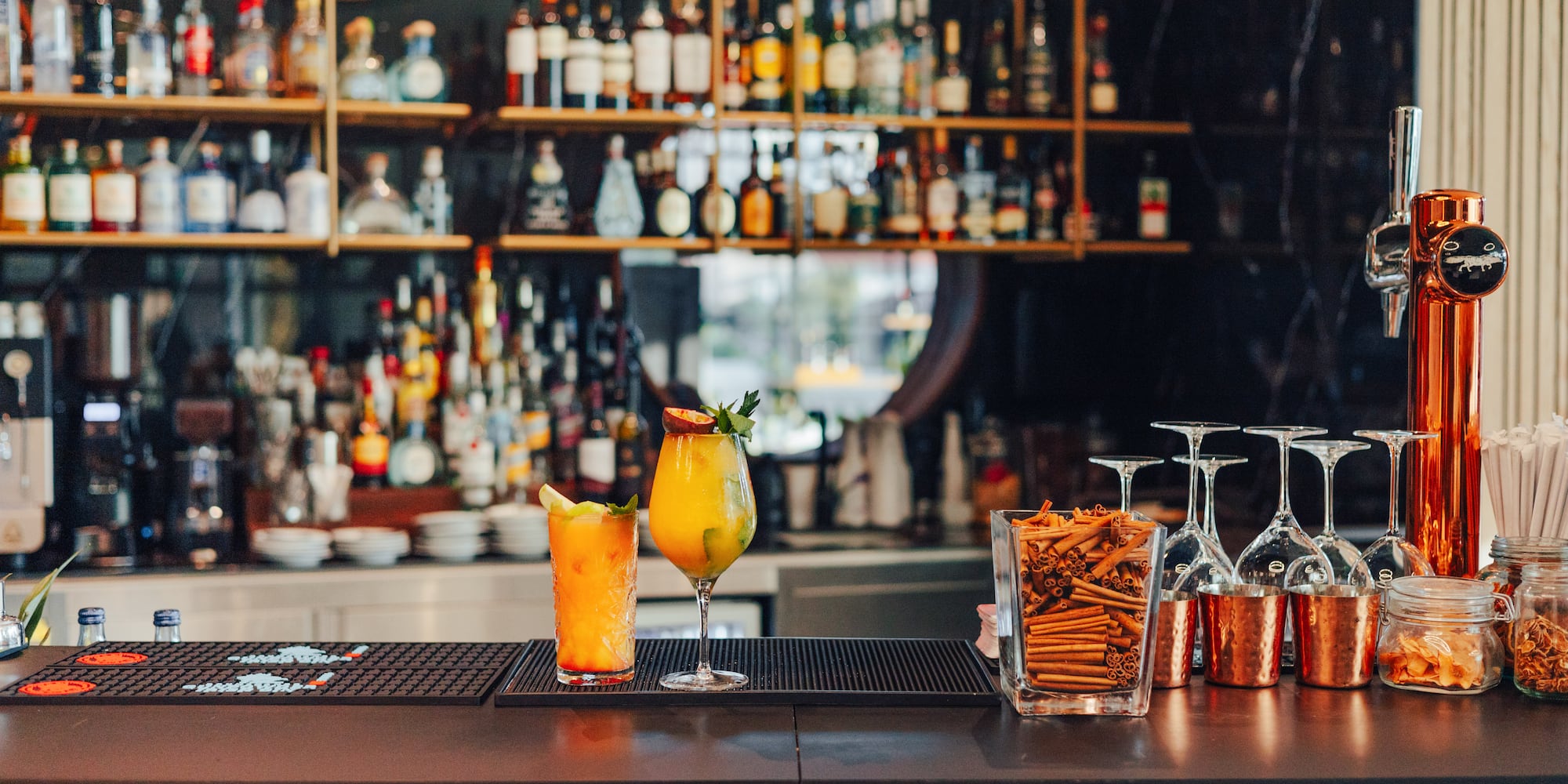 Vibrant cocktails on a modern bar counter with liquor bottles in background.