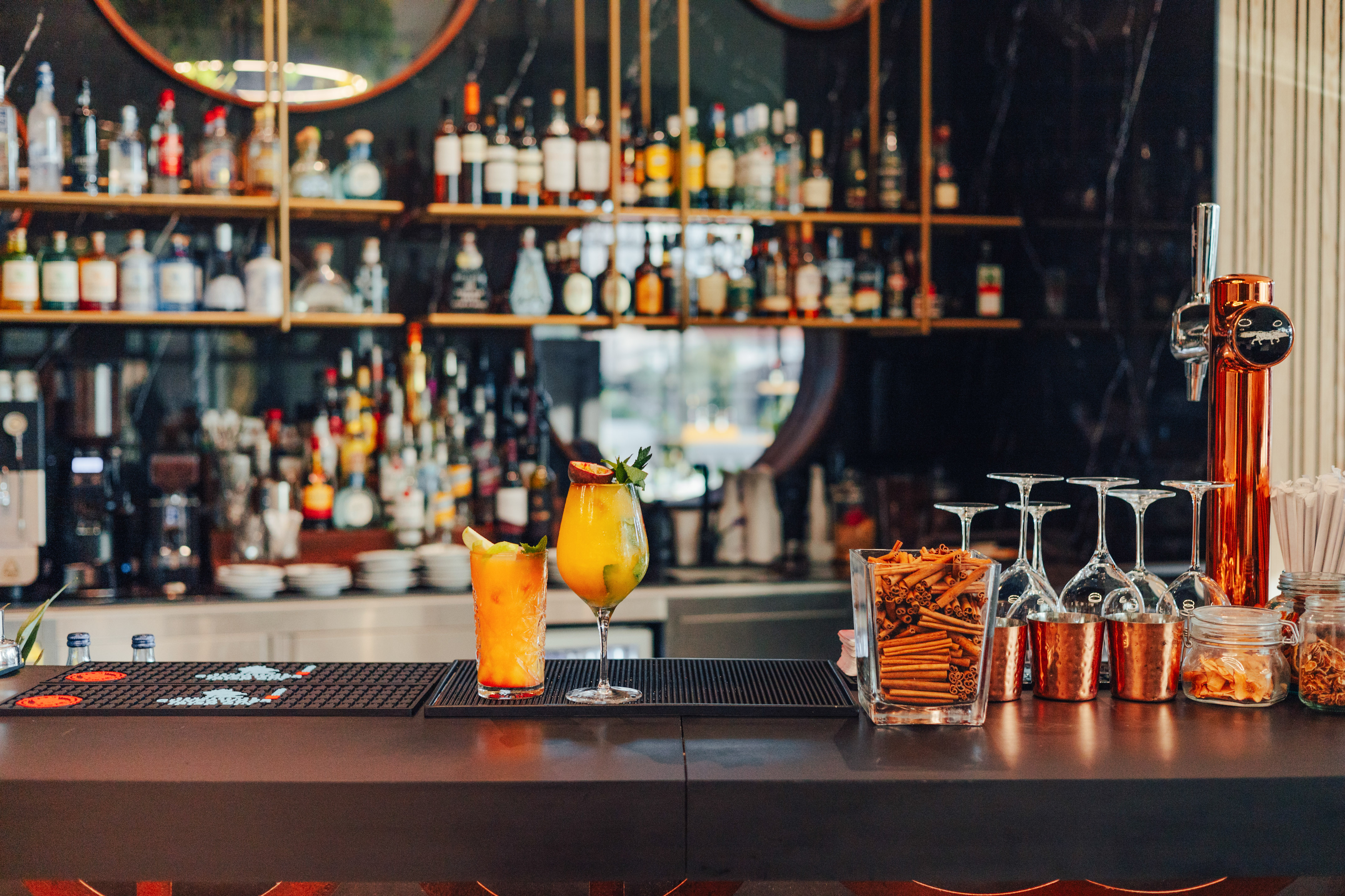 Vibrant cocktails on a modern bar counter with liquor bottles in background.