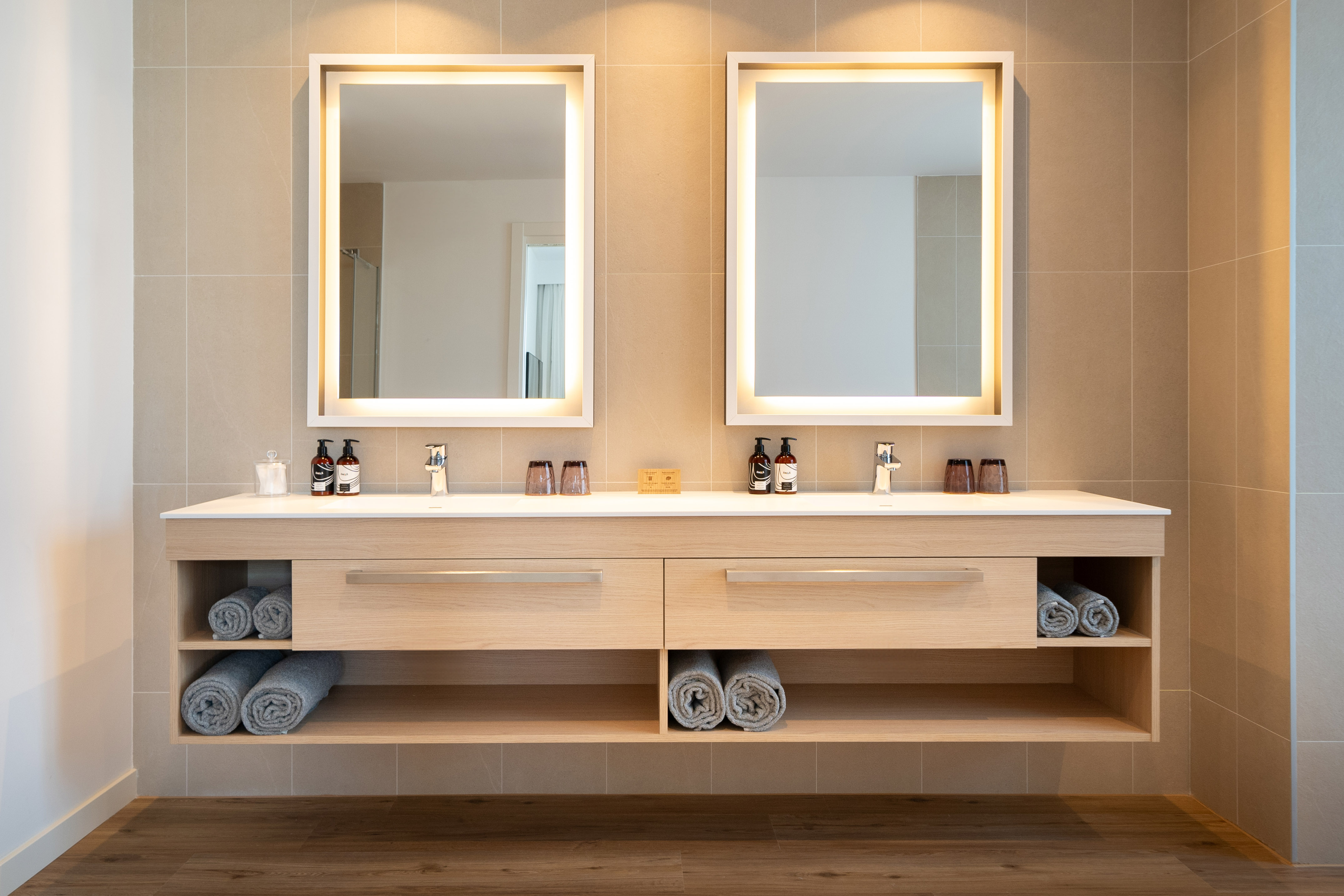 Modern double vanity bathroom with lighted mirrors and wooden cabinet.