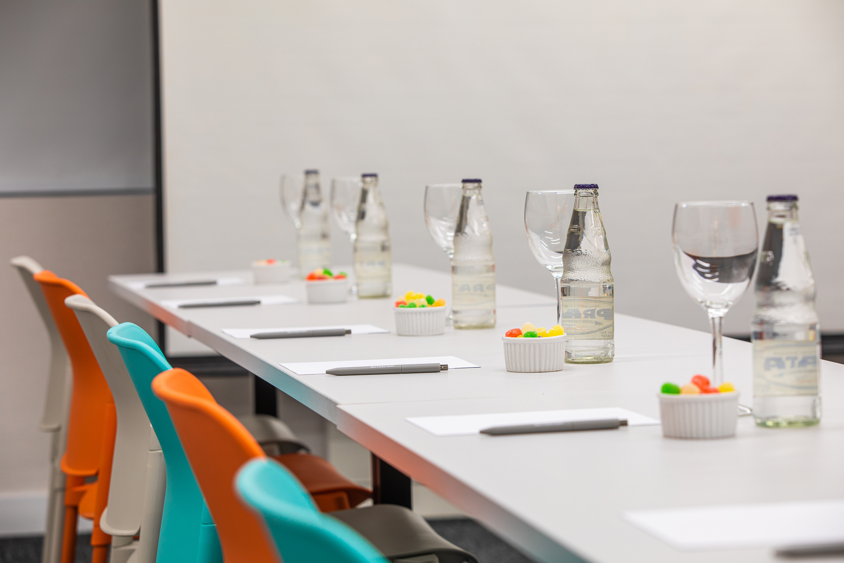 Meeting table with colorful chairs, water bottles, glasses, and jelly candies.