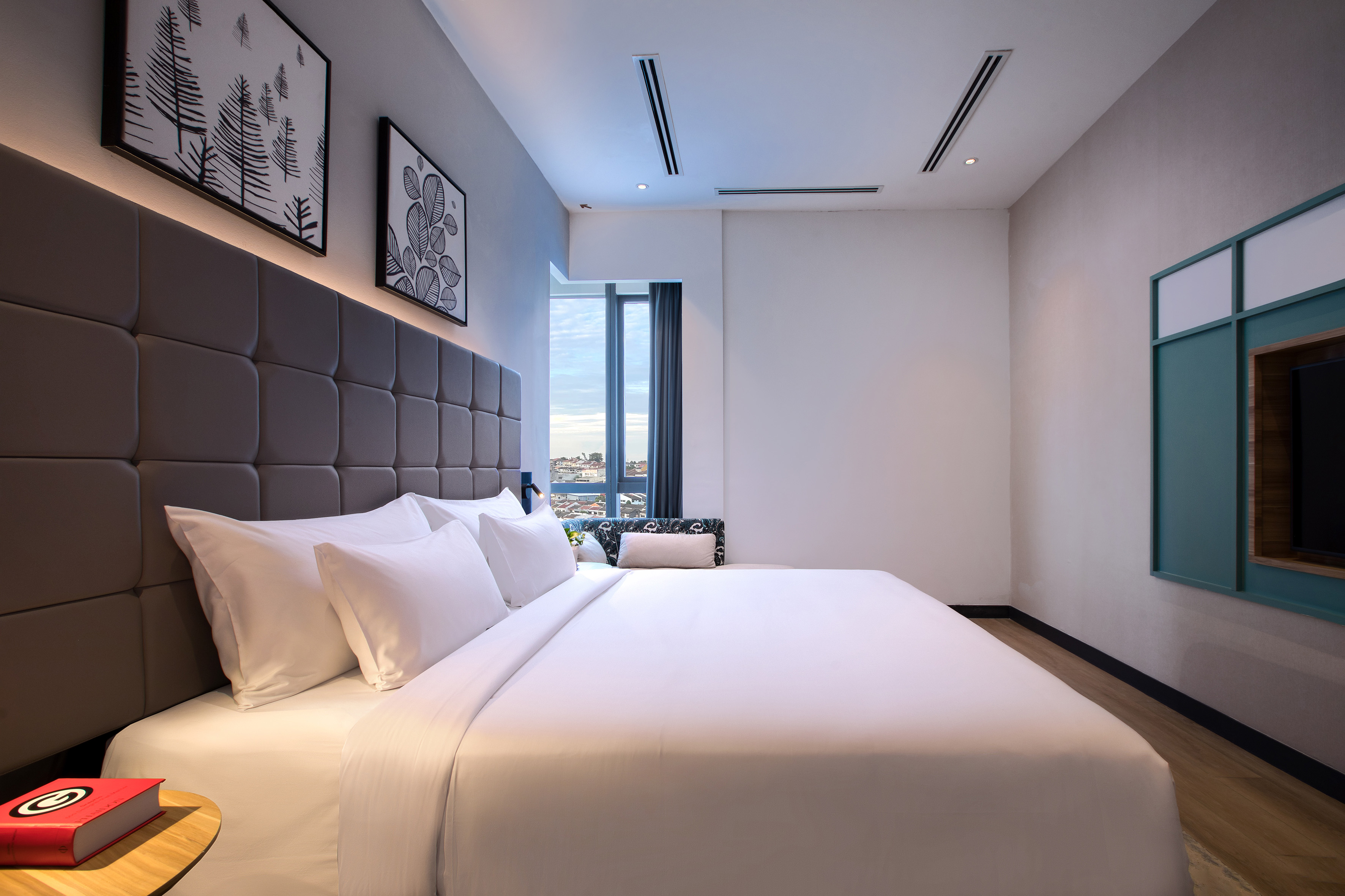 Modern hotel bedroom with large white bed, gray tufted headboard, city view.