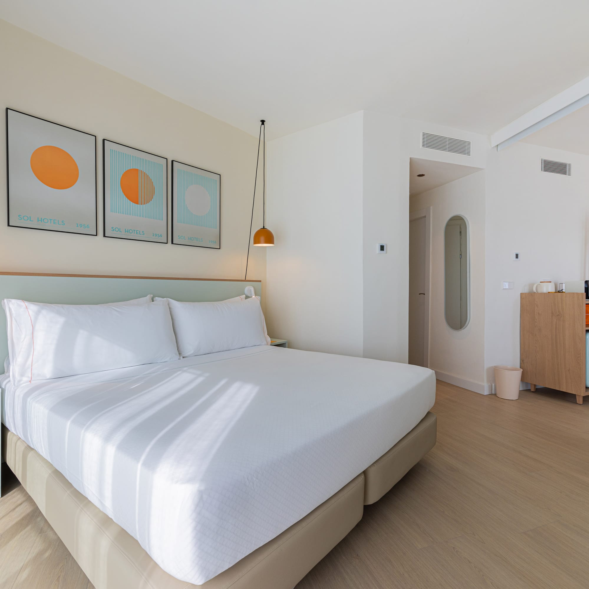 Modern hotel room with white bed, light green headboard, and minimalist art.