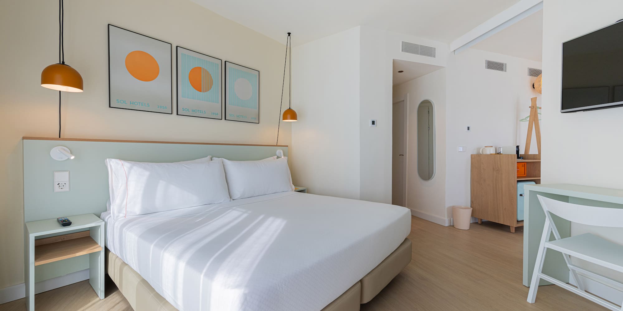 Modern hotel room with white bed, light green headboard, and minimalist art.